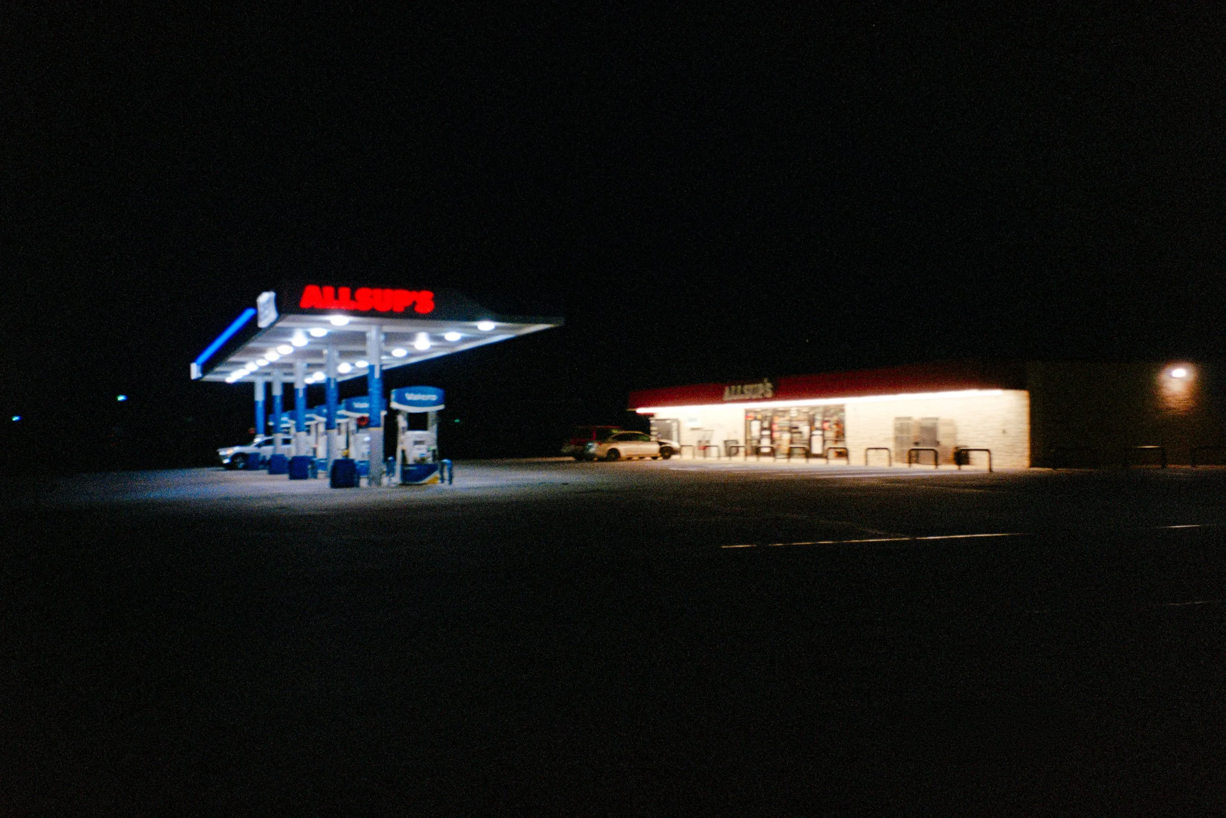 A deserted Allsup's gas station at night with illuminated pumps and a small store