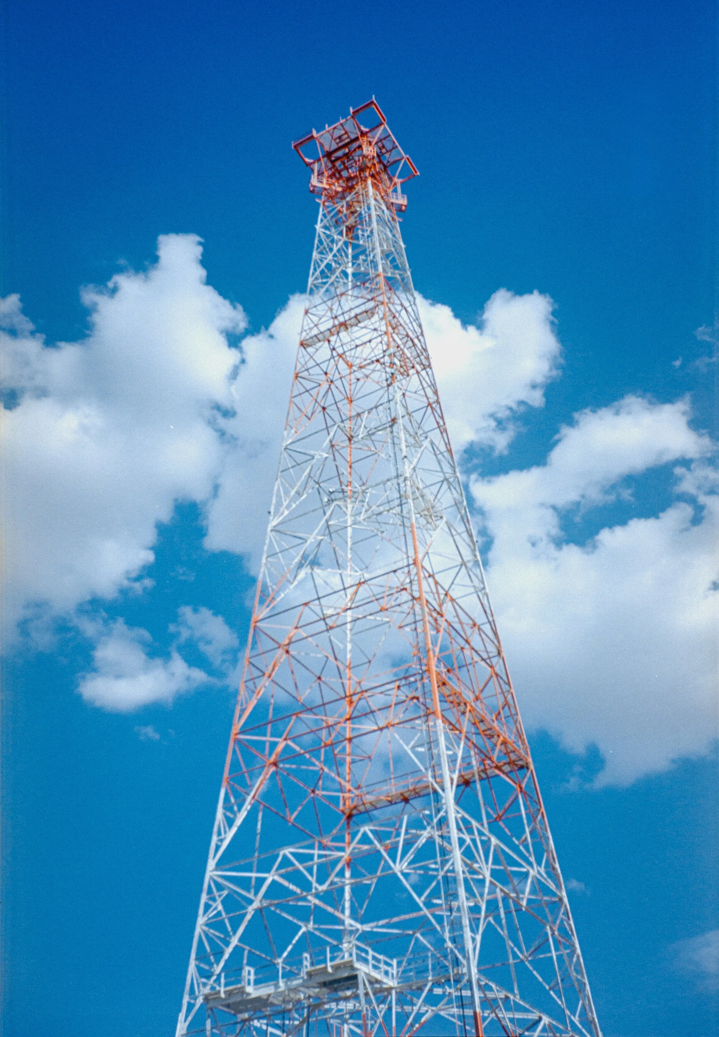 Tall radio tower painted in red and white against a blue sky with white clouds.