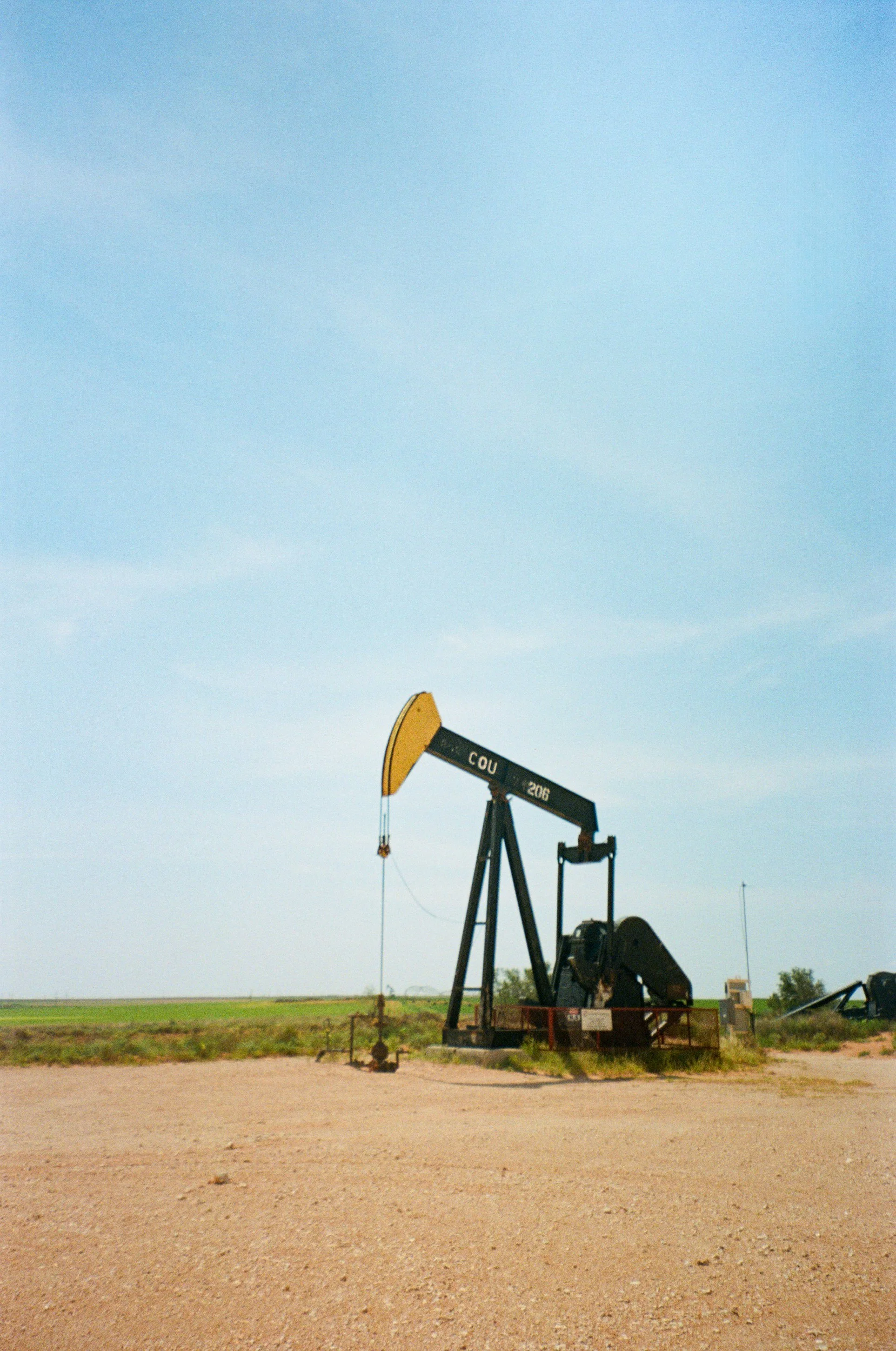 An oil pumpjack in a flat, open landscape under a clear blue sky.
