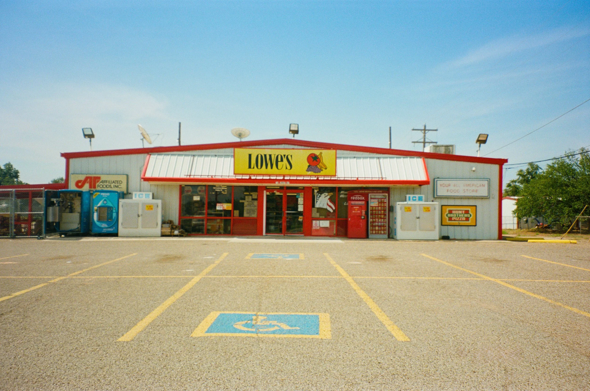 Front view of a Lowe's store with a parking lot, including designated handicap parking spaces, under a blue sky.