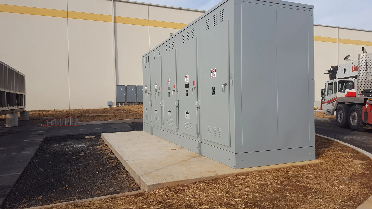 Large outdoor electrical equipment enclosure beside a commercial building