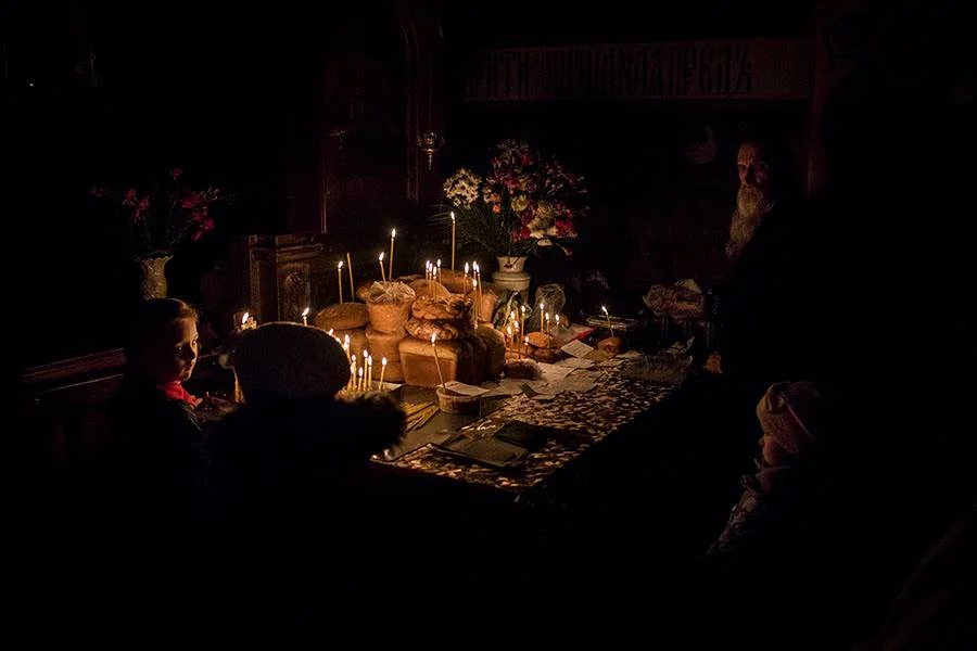Manu Brabo, Ukranian kids stand around a table full of cakes while an orthodox priest watch after it during an early morning mass , 2019, digital printing, courtesy Manu Brabo/ Raffaella De Chirico Arte Contemporanea