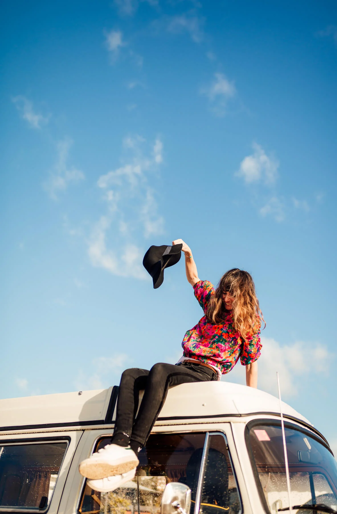Jo Kemp photographer enjoying life on top of a VW van taking her hat off