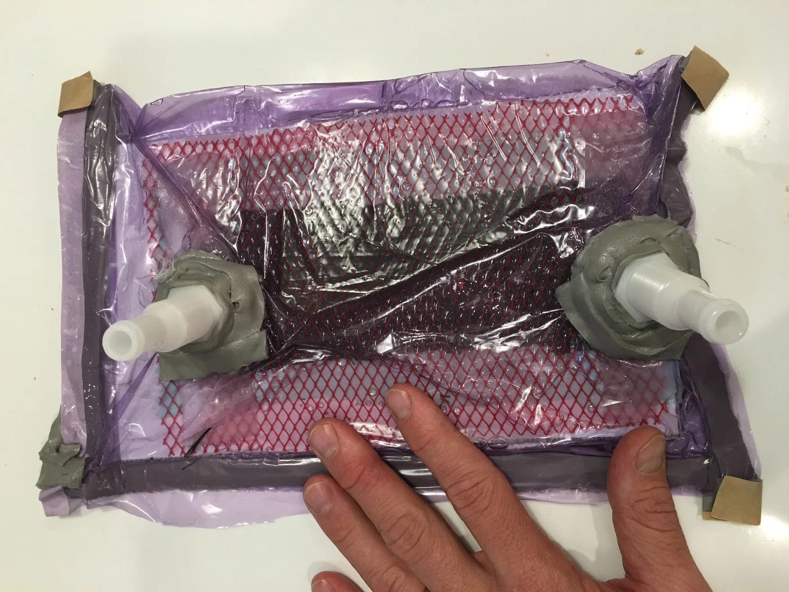 Carbon fiber layup ready for vacuum infusion. Inlet (resin) and outlet (vacuum) ports are visible.