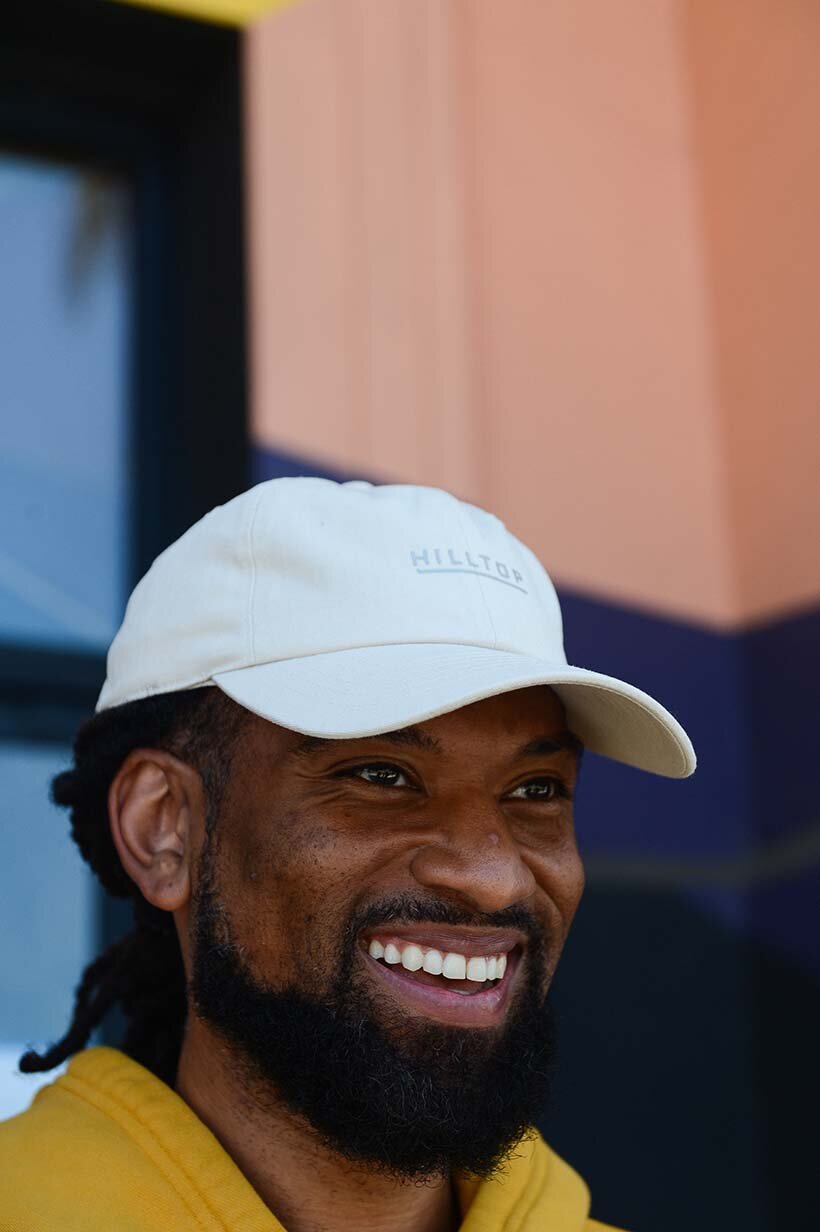 Man smiling and wearing a white Hilltop hat