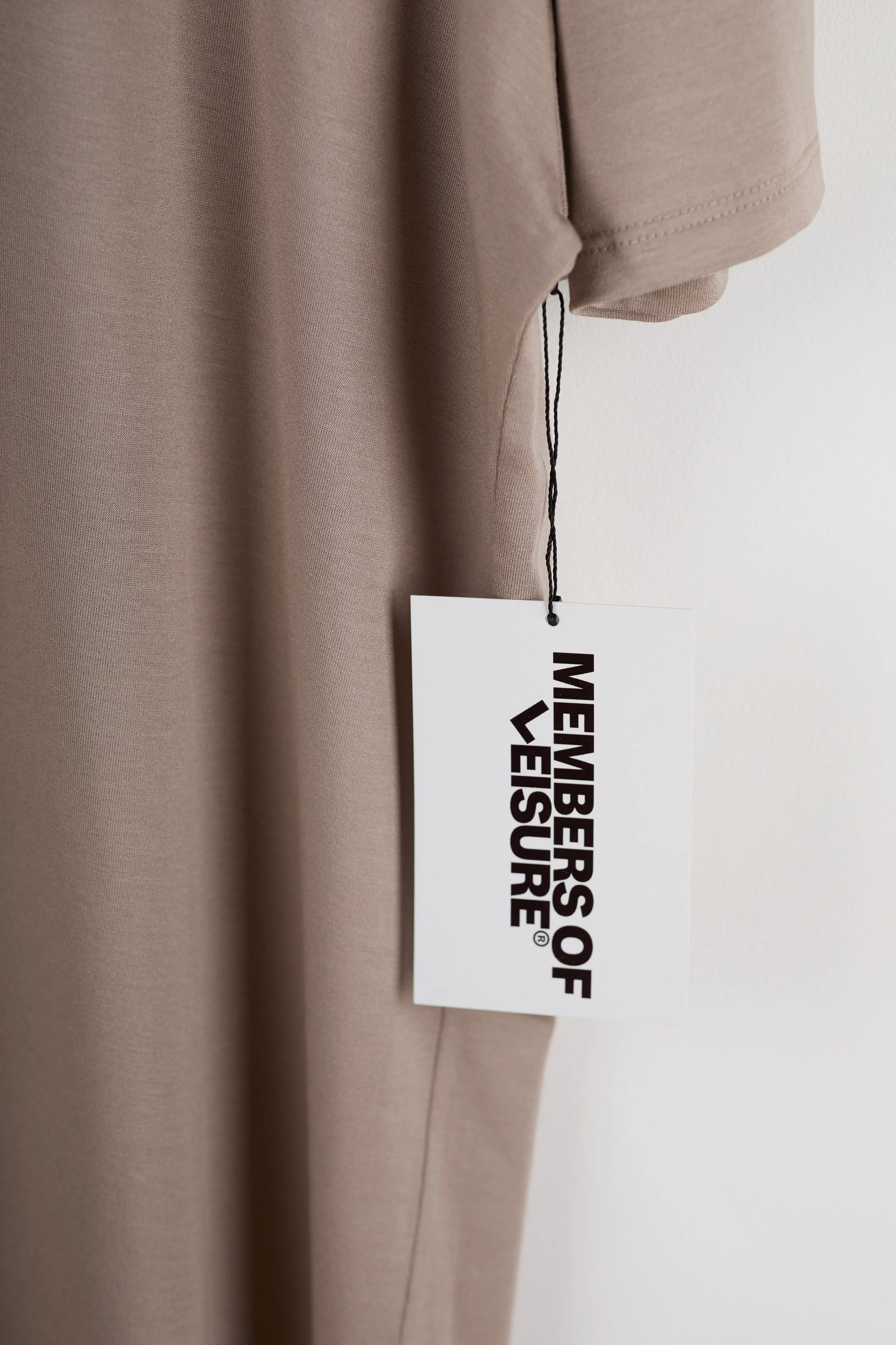 Close-up of beige clothing with a white tag hanging, reading 'Members of the VELV₲RE' in bold black letters.