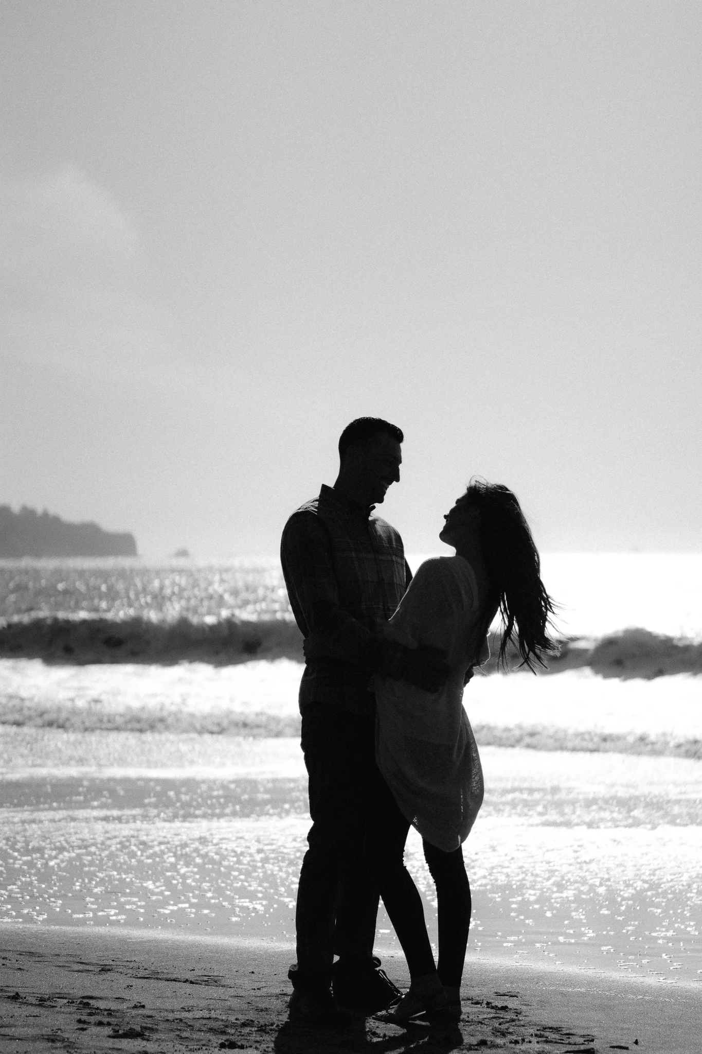 Engaged couple writing their initials in the sand at Baker Beach in San Francisco during their romantic sunset photo shoot celebrating their engagement.