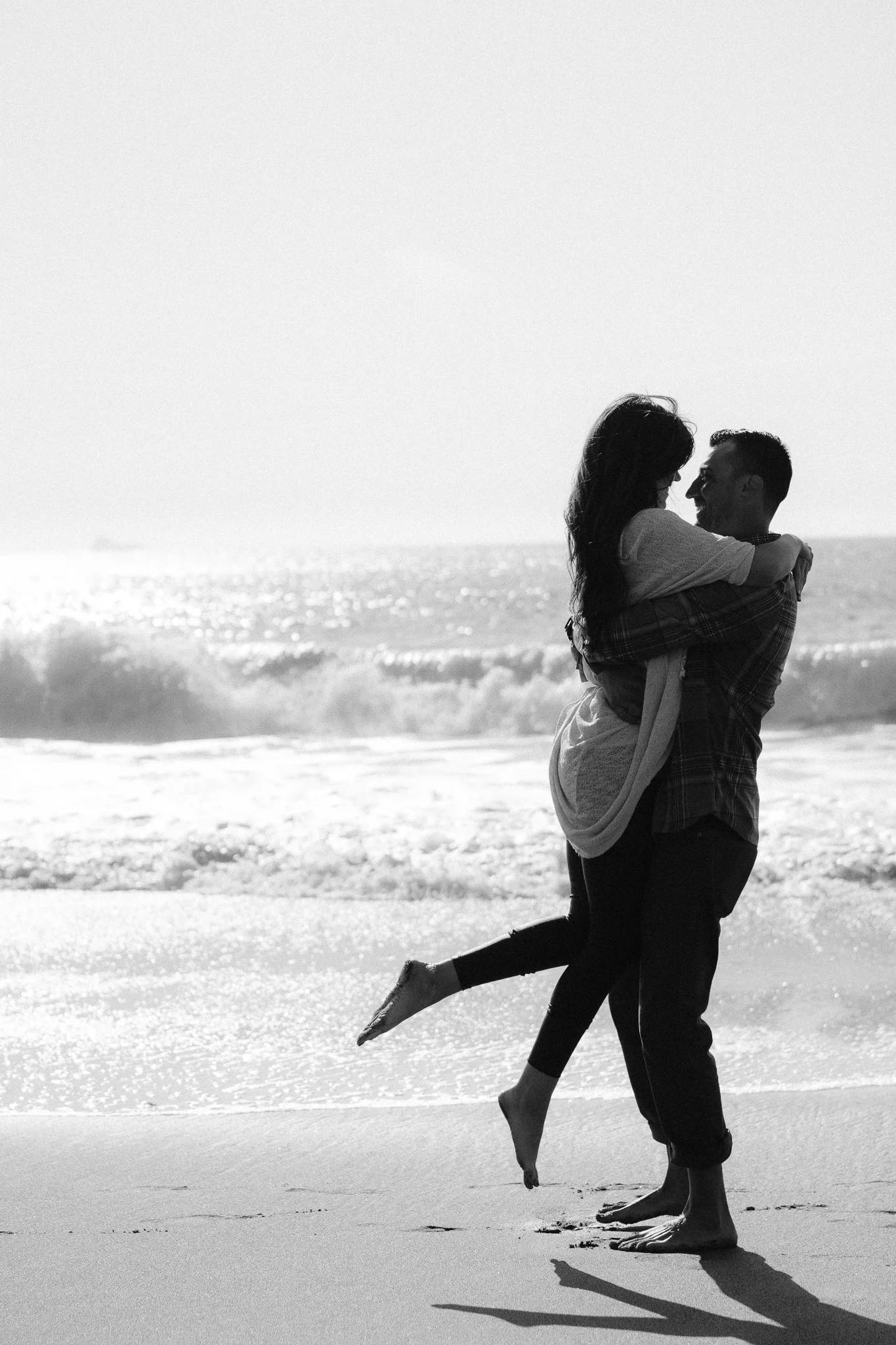 Romantic black and white beach engagement photo of couple embracing on Baker Beach in San Francisco.