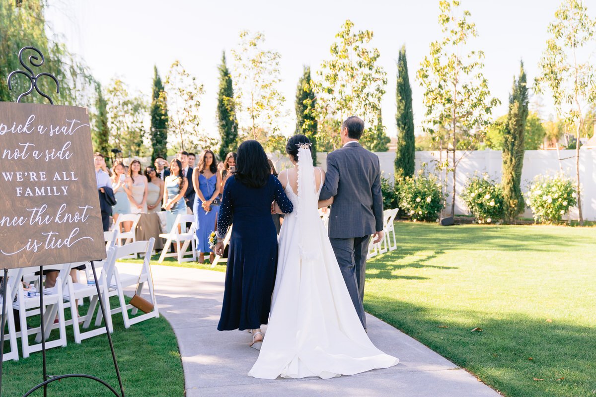 Rear view of bride walking down the aisle at San Ramon Waters with her mom and dad by her side