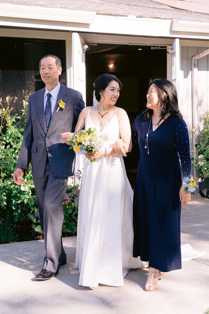 Bride walking down the aisle at San Ramon Waters with her mom and dad by her side