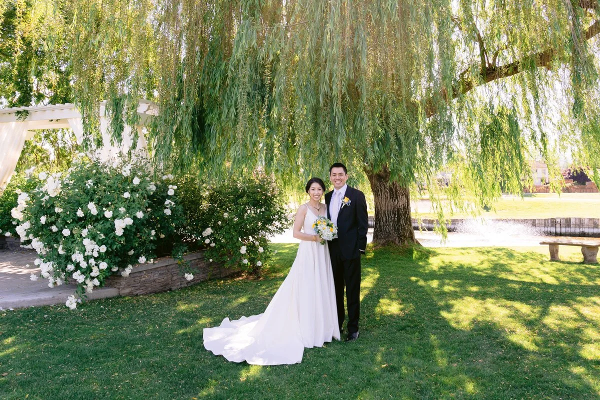 Bride and groom posing for wedding photo underneath a weeping willow tree at San Ramon Waters by Wedgewood Weddings