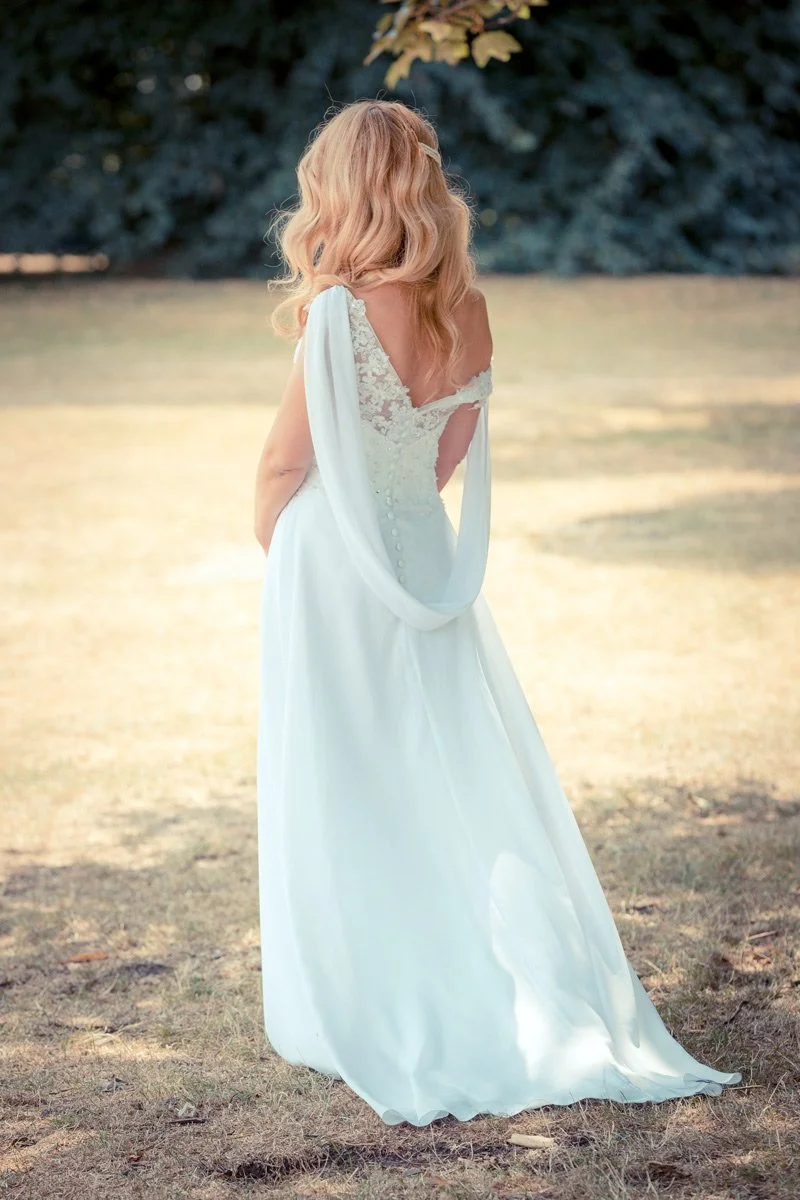 Bride standing outdoors in a garden, facing away with long blonde hair cascading down her back.