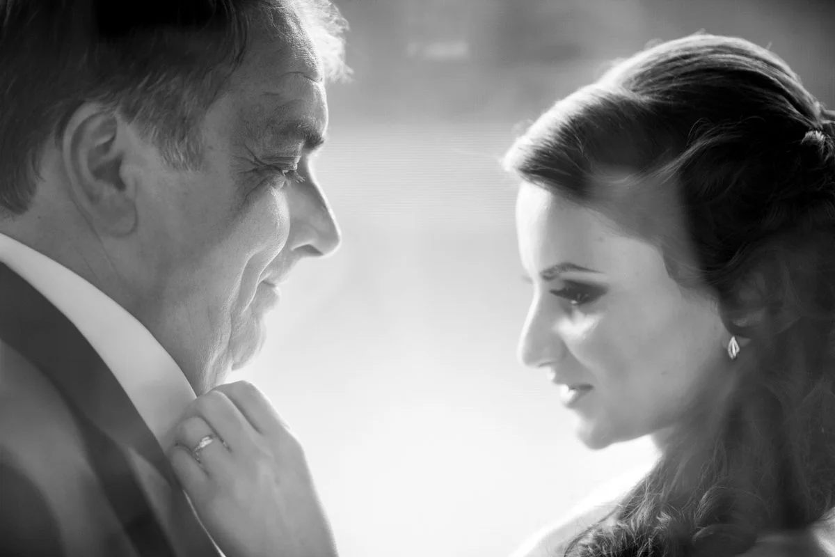 Black and white photo of bride and her father facing each other, the bride adjusting her father's collar.