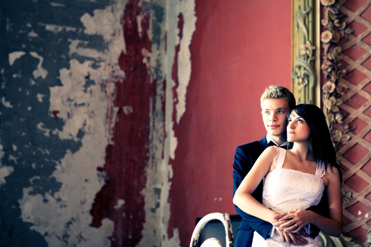 A couple embracing in formal attire against a textured wall backdrop.