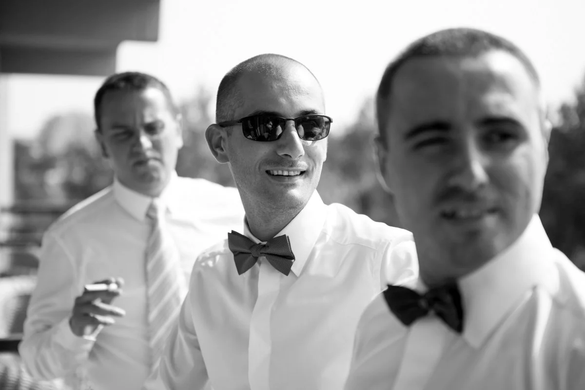Three men in formal attire, wearing bow ties, standing outdoors; one man is wearing sunglasses. The image is in black and white.