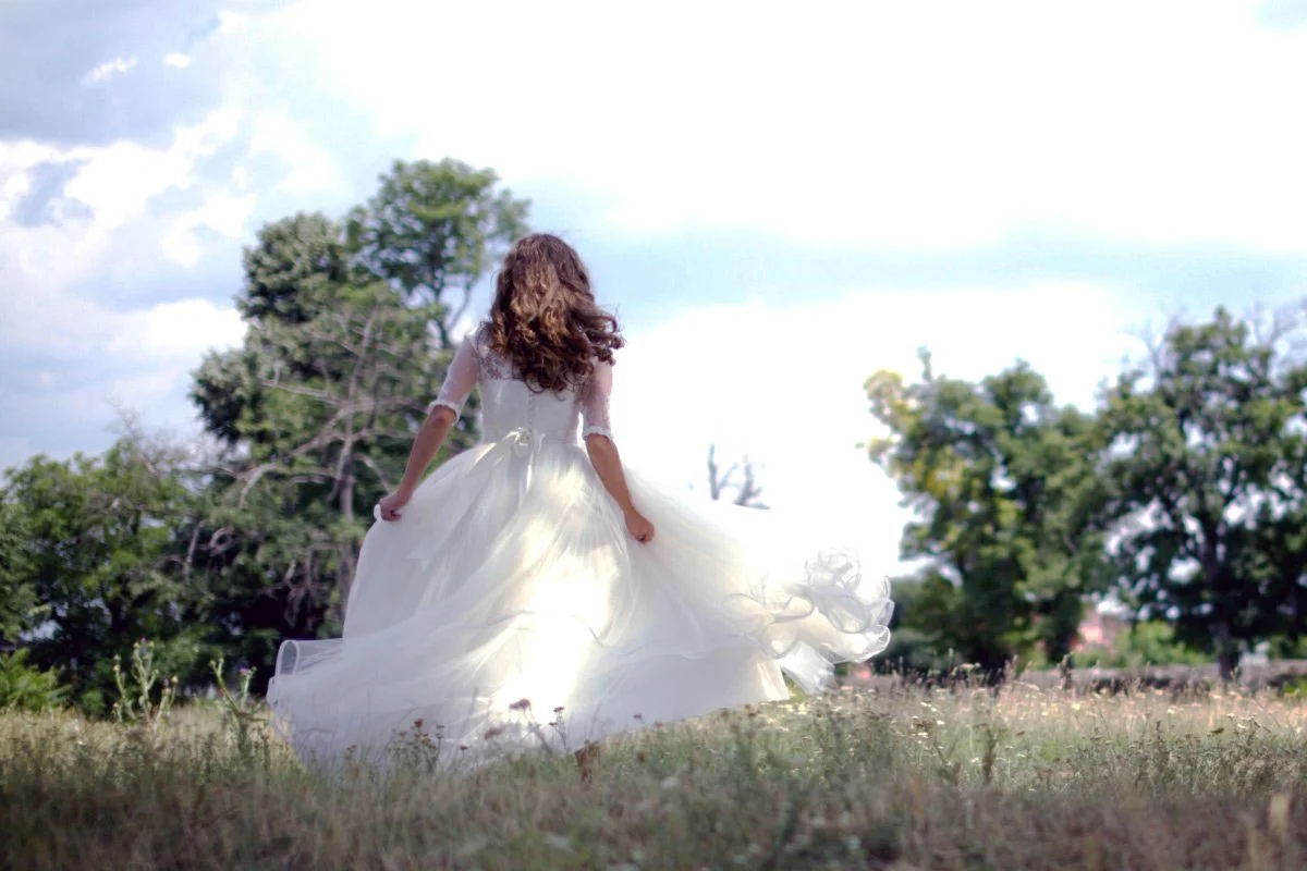 Bride running in a field with trees in the background.