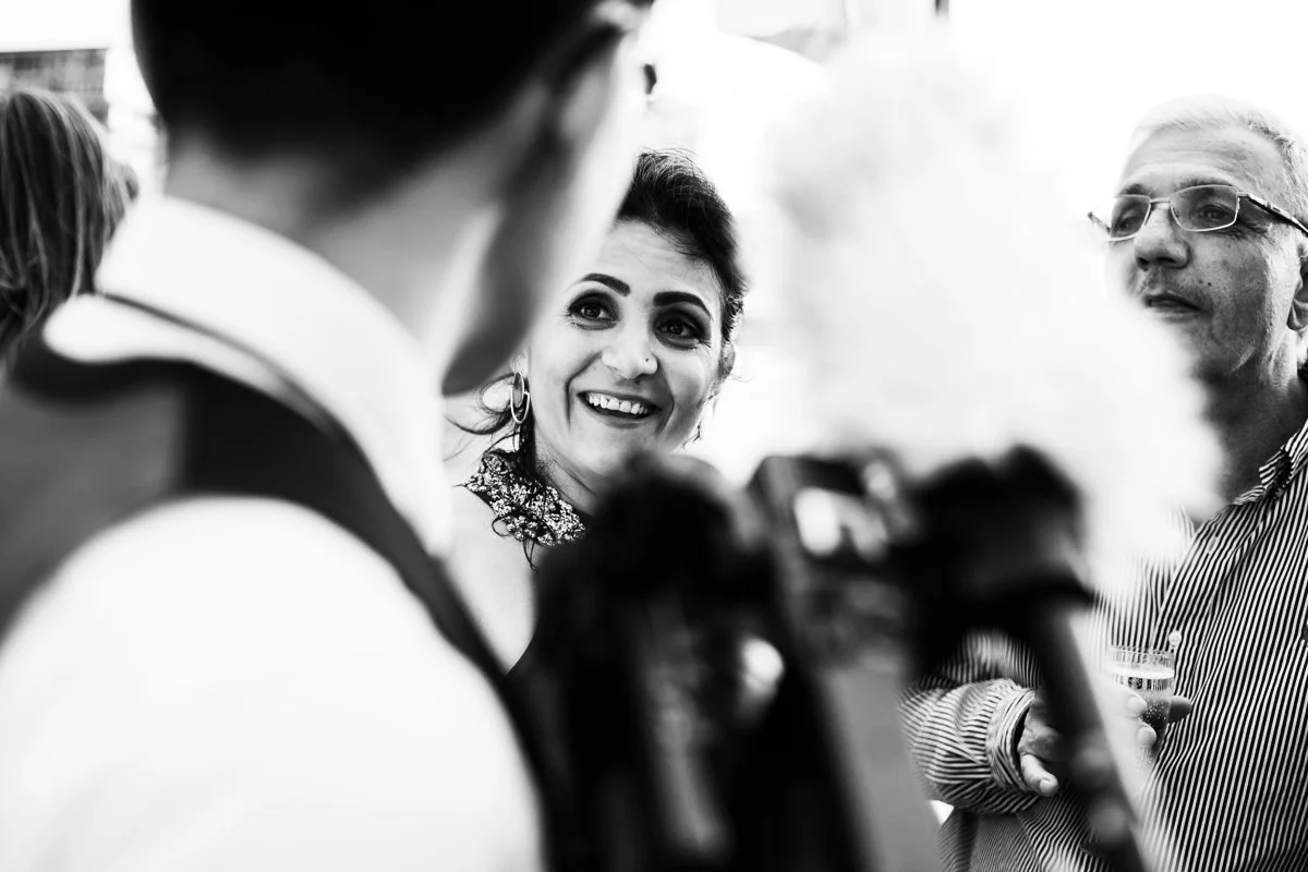 Black and white photo of a woman smiling and a man wearing glasses, engaged in conversation at a wedding.