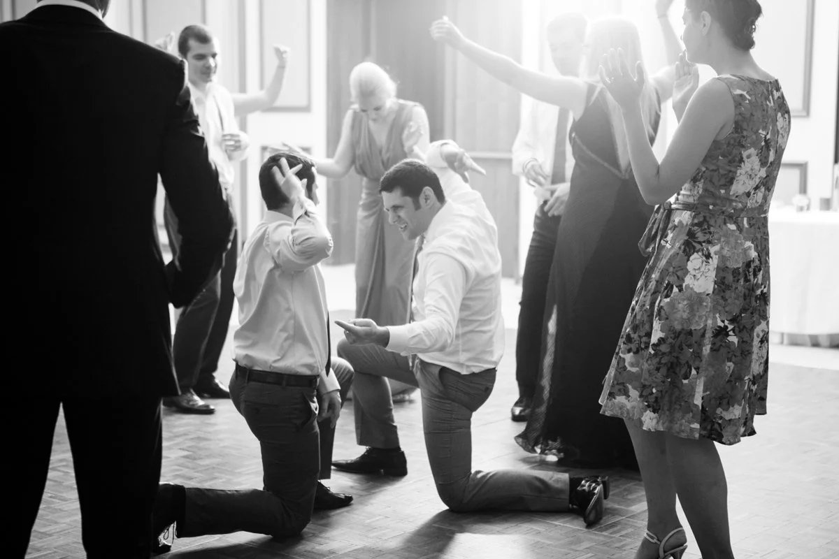 A black and white photo of people dancing at a wedding party, with guests in various poses and expressions of joy on the dance floor.