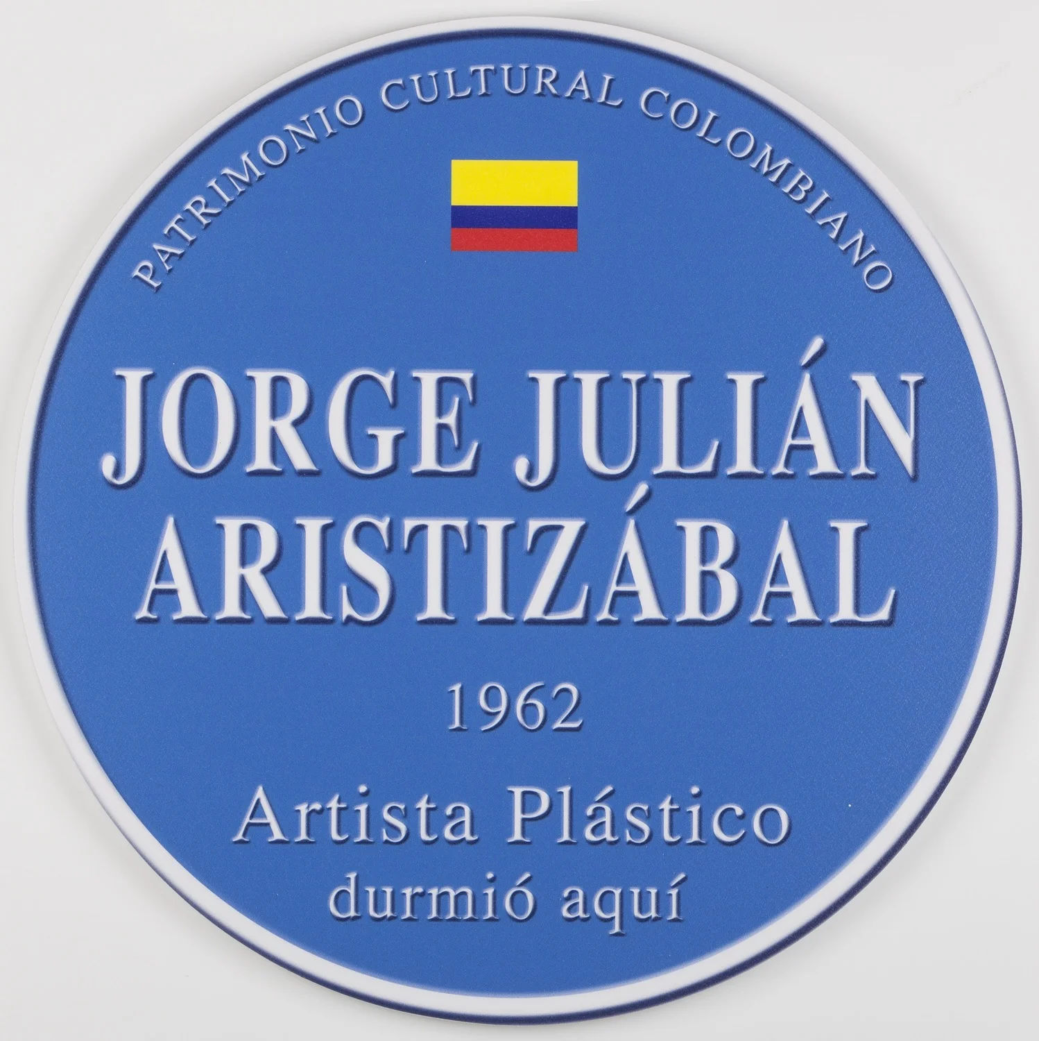 Placa conmemorativa Por medio del humor, Aristizábal aborda la invisibilidad del artista en Colombia, así como el olvido y la apatía que viven las entidades culturales. Estas placas recuerdan las que se colocan en Inglaterra sobre las fachadas de edificios en las que vivieron artistas o personajes famosos de la cultura, pero a diferencia de las inglesas –fundidas en bronce y con un alto grado de decoro–éstas son plásticas y conmemoran acciones mundanas tales como comer y dormir. Impresión digital sobre plástico, 35 cm de diámetro 2014