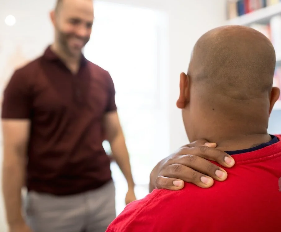 A person holding their neck during a consultation at ONE80 Health in Toronto