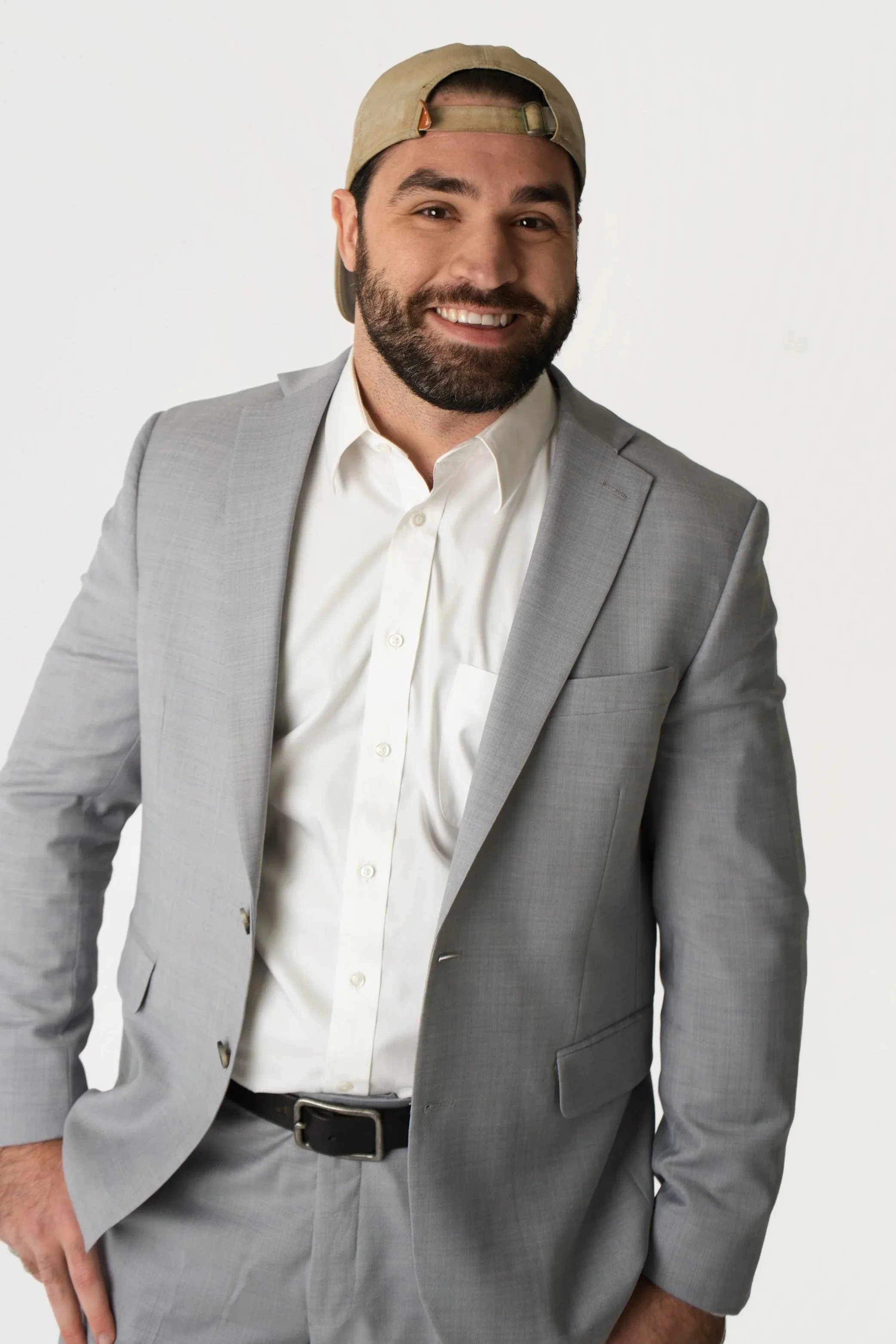 Professional portrait of a young man in a navy suit, white shirt, and patterned tie, with dark hair and a friendly smile, against a neutral background.