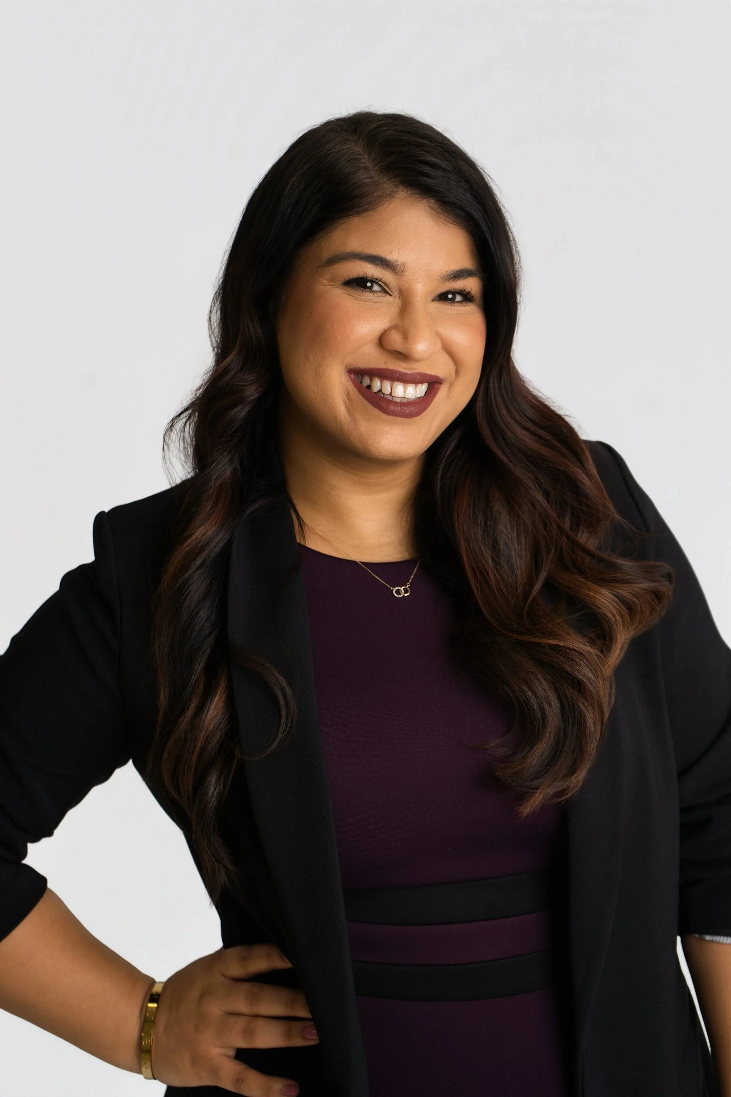 A professional woman with straight black hair, light makeup, wearing a blue blazer and black shirt, smiling confidently at the camera.