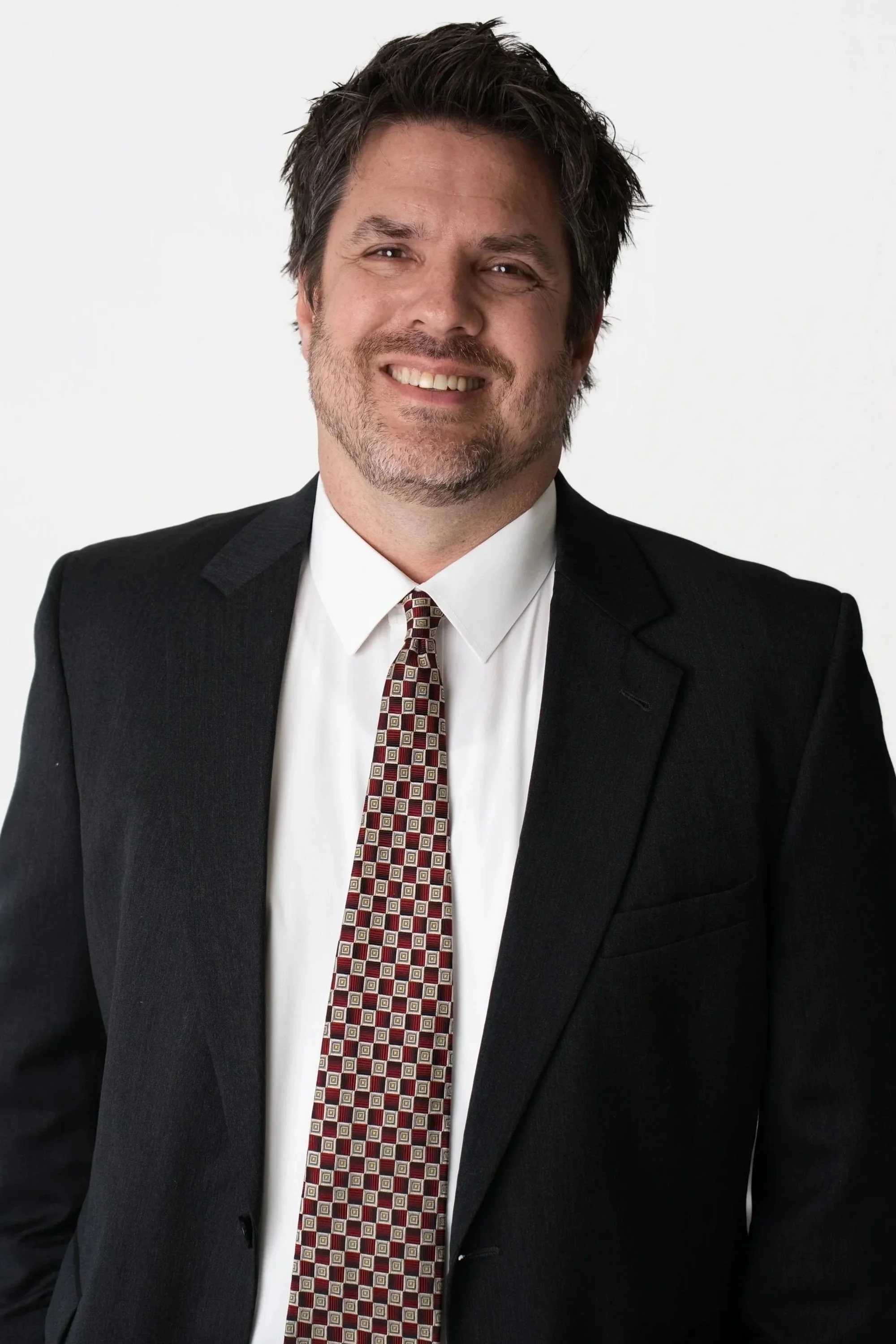 A portrait of a man with brown hair, light skin, wearing a lavender dress shirt and a patterned tie, against a neutral background.