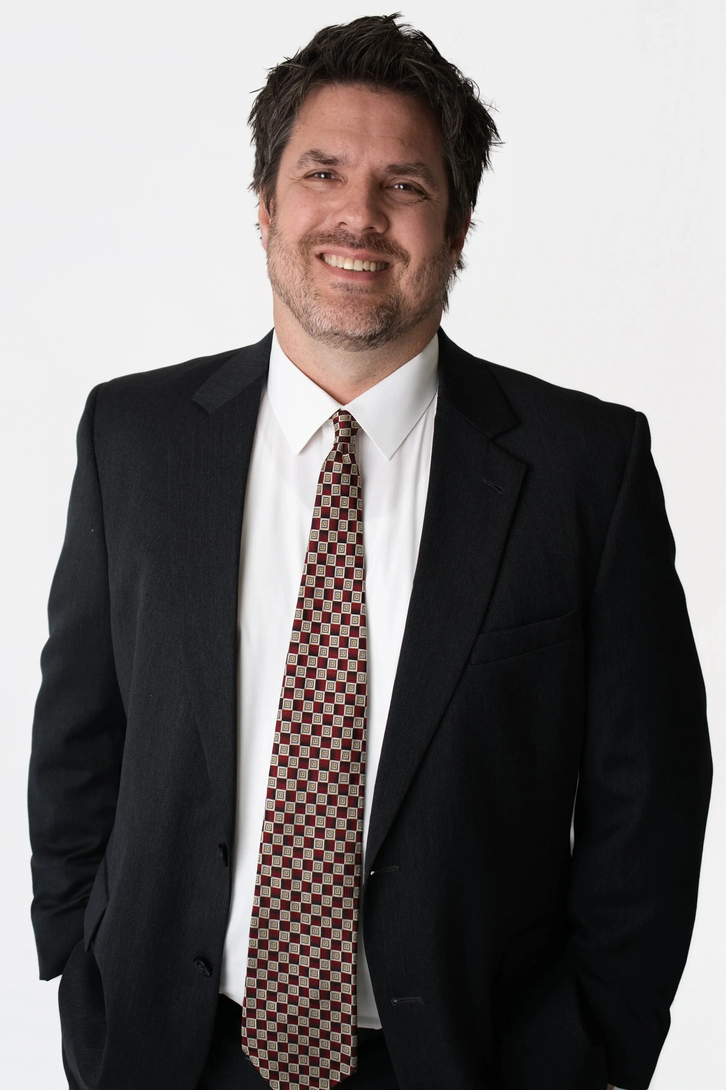 A portrait of a man with brown hair, light skin, wearing a lavender dress shirt and a patterned tie, against a neutral background.