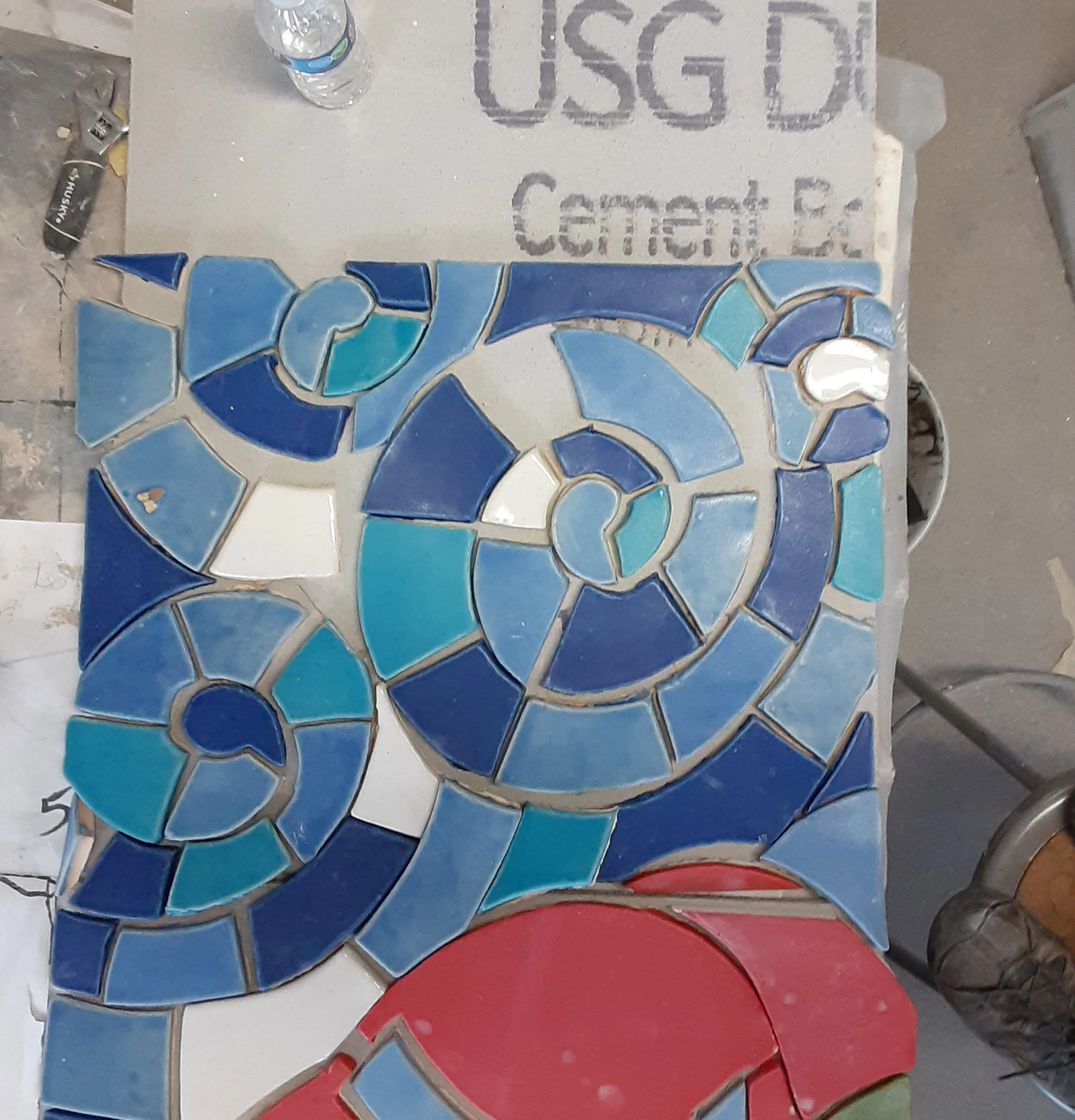 Hand-glazed blue ceramic tiles arranged in a spiral pattern for a Whistling Frog Tile mural.