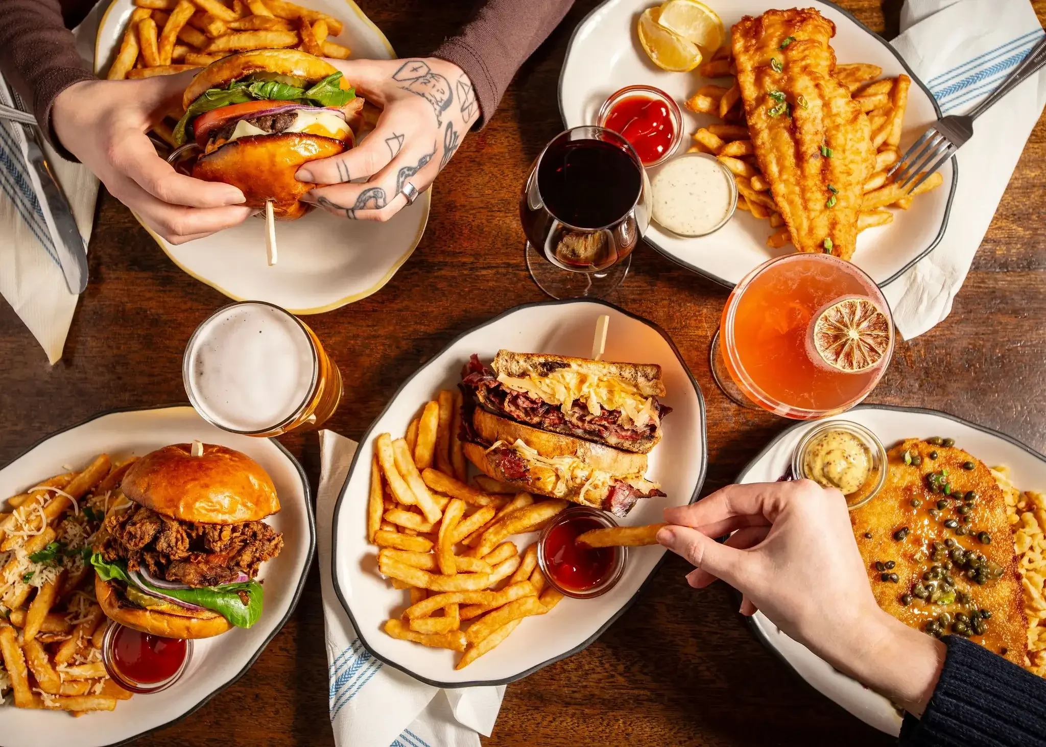 A top down shot of various dishes at the Dutch Ale House in Saugerties, NY. A burger, fried fish and chips, a fried chicken sandwich, chicken piccata, a reuben sandwich, and various cocktails and beer. 