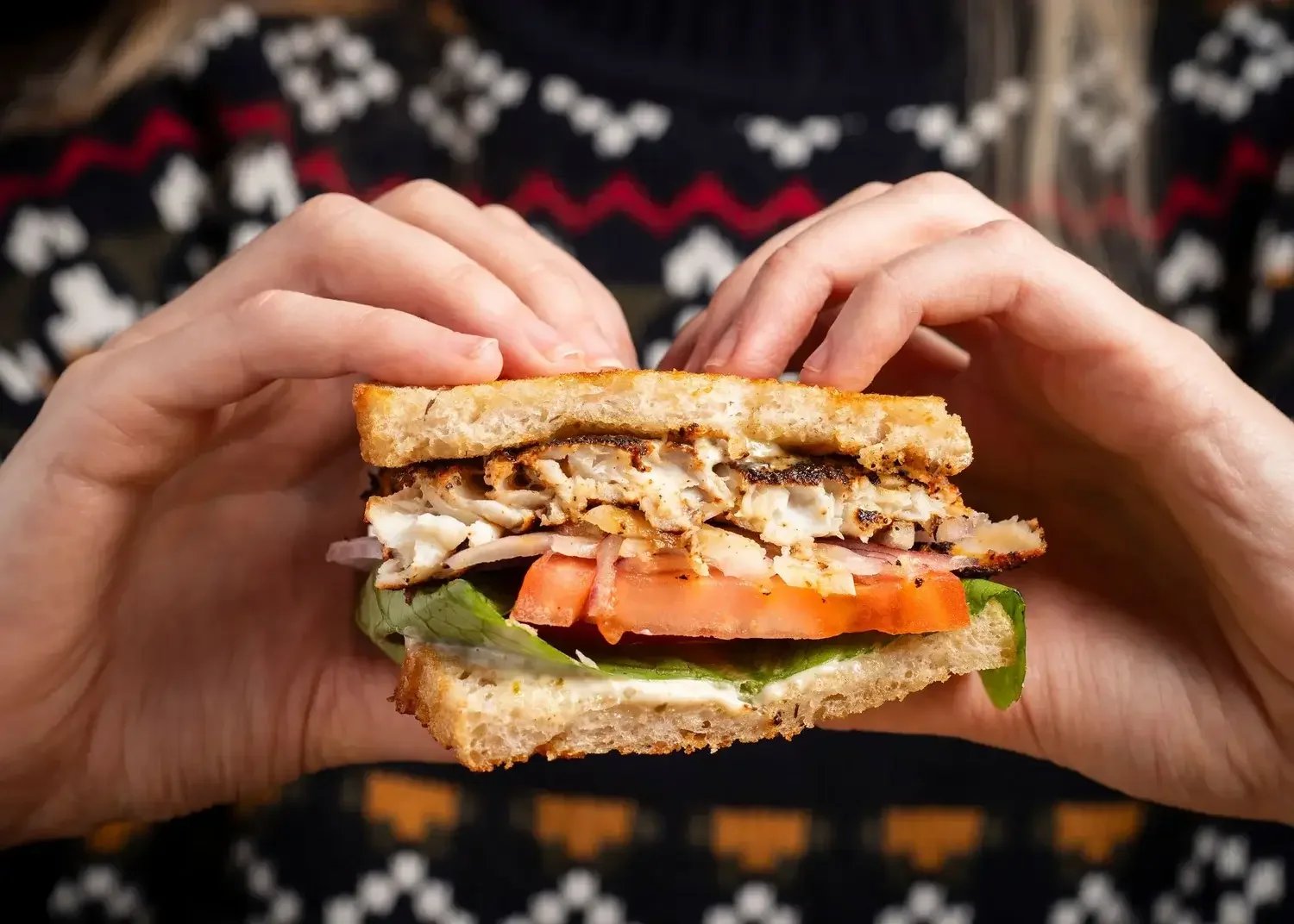 A person holding a chicken sandwich with lettuce and tomato on white bread, made fresh at the Dutch Ale House in Saugerties, NY.