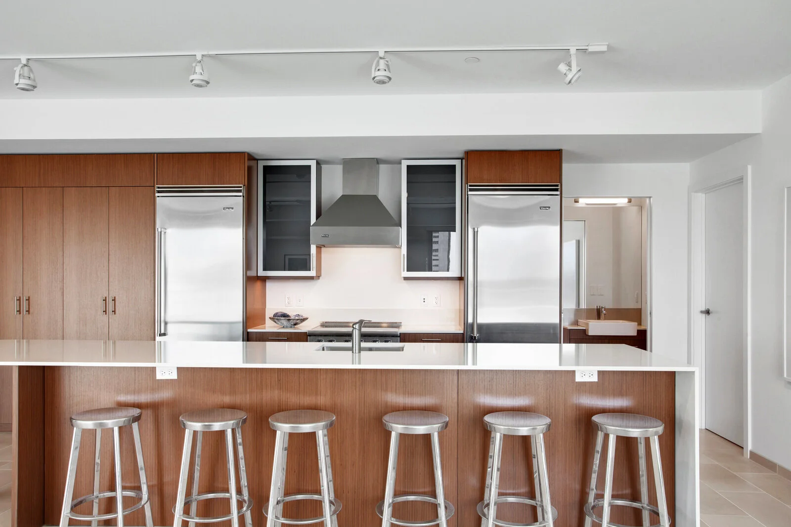  Luxury New Orleans, LA, Apartments For Rent - The Garage - Kitchen With Sleek Light Fixtures, Stool Chairs, Wood-Like Cabinets, Stainless Steel Appliances, and White Countertops 