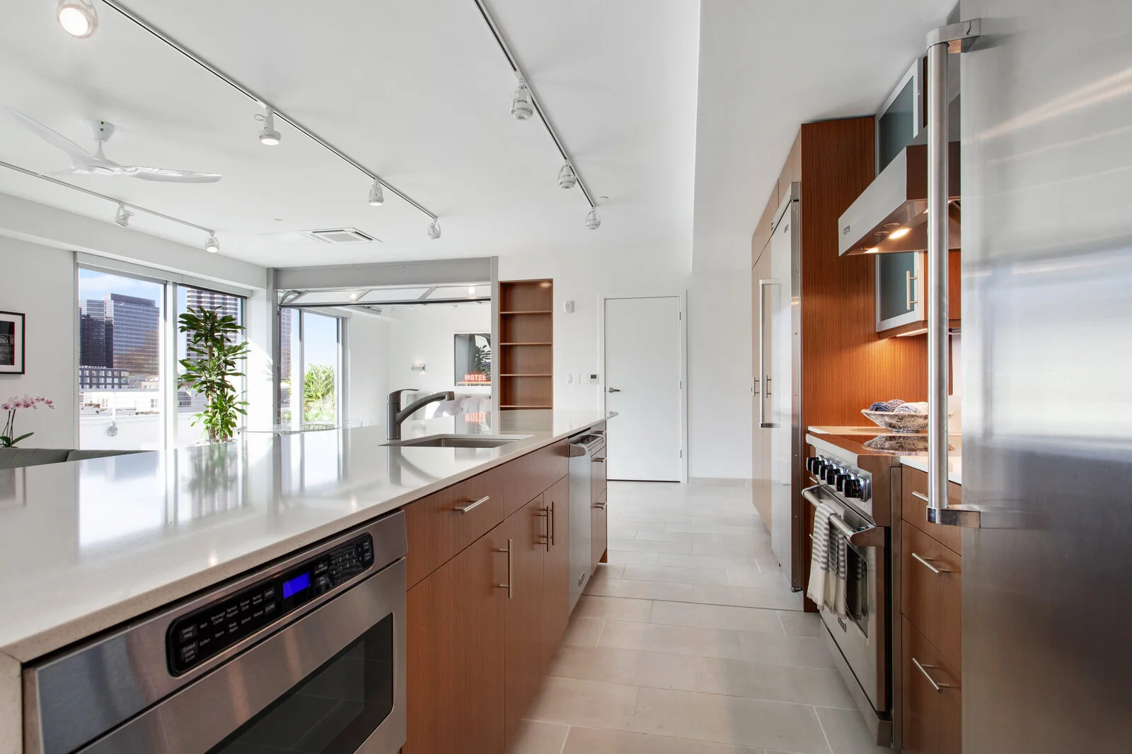 Warehouse District LA Apartments - The Garage - Modern Kitchen with Wood-Style Cabinetry, White Quartz Countertops, Stainless Steel Appliances, White Tile Flooring, Lots of Light From Large Windows, and Open-Concept Layout 