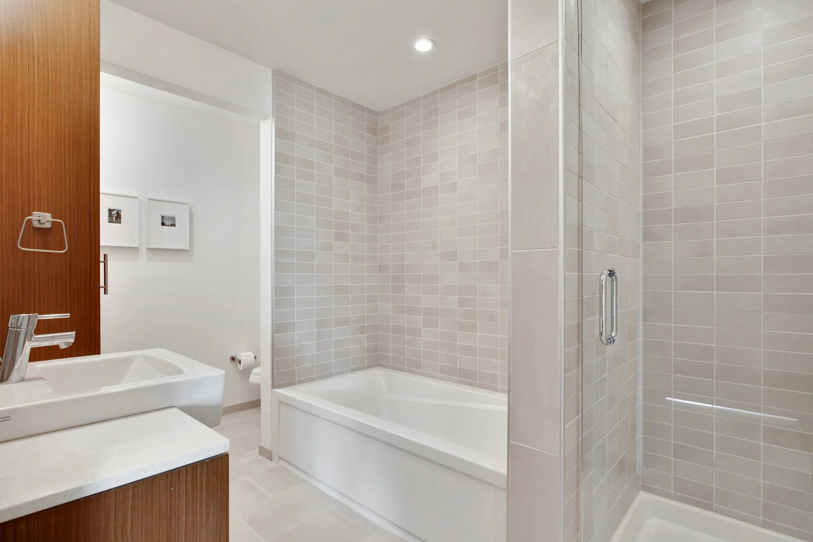  Luxury Apartments in New Orleans, LA For Rent - The Garage - Bathroom With Puck Lighting, White Countertops, White Tub, Wall Art, High Ceilings, Wood-Like Cabinetry, and Glass Door. 