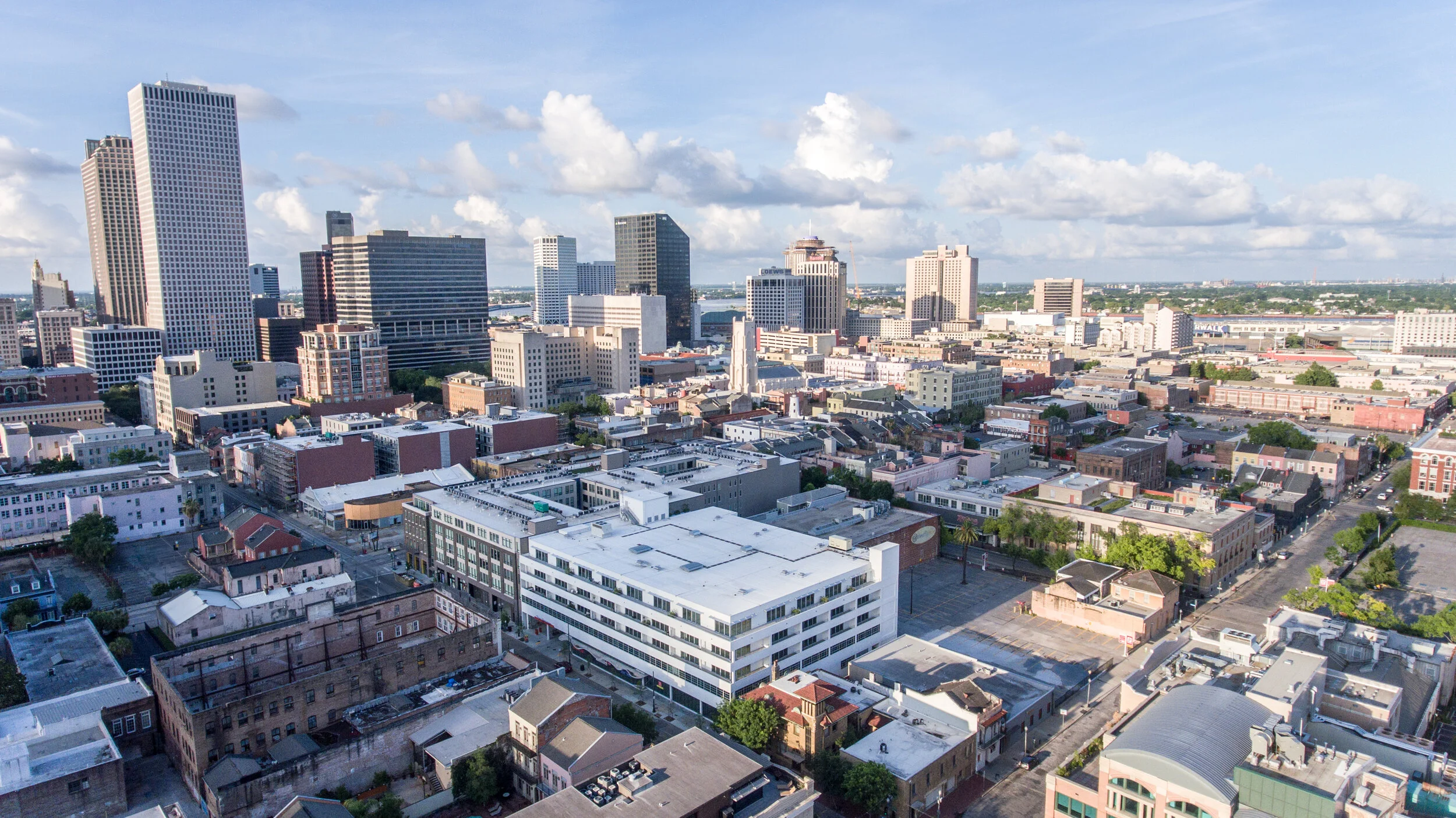  Luxury New Orleans LA Apartments for Rent - The Garage - Bird's Eye Drone View of Property Exterior and Surrounding Neighborhood, with Downtown in the Background, with White Walls and Nearby Trees 
