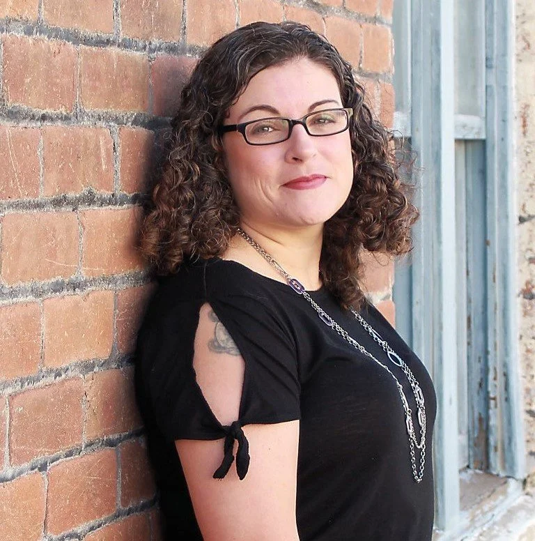 Samantha wearing a black shirt leaning against a red brick wall
