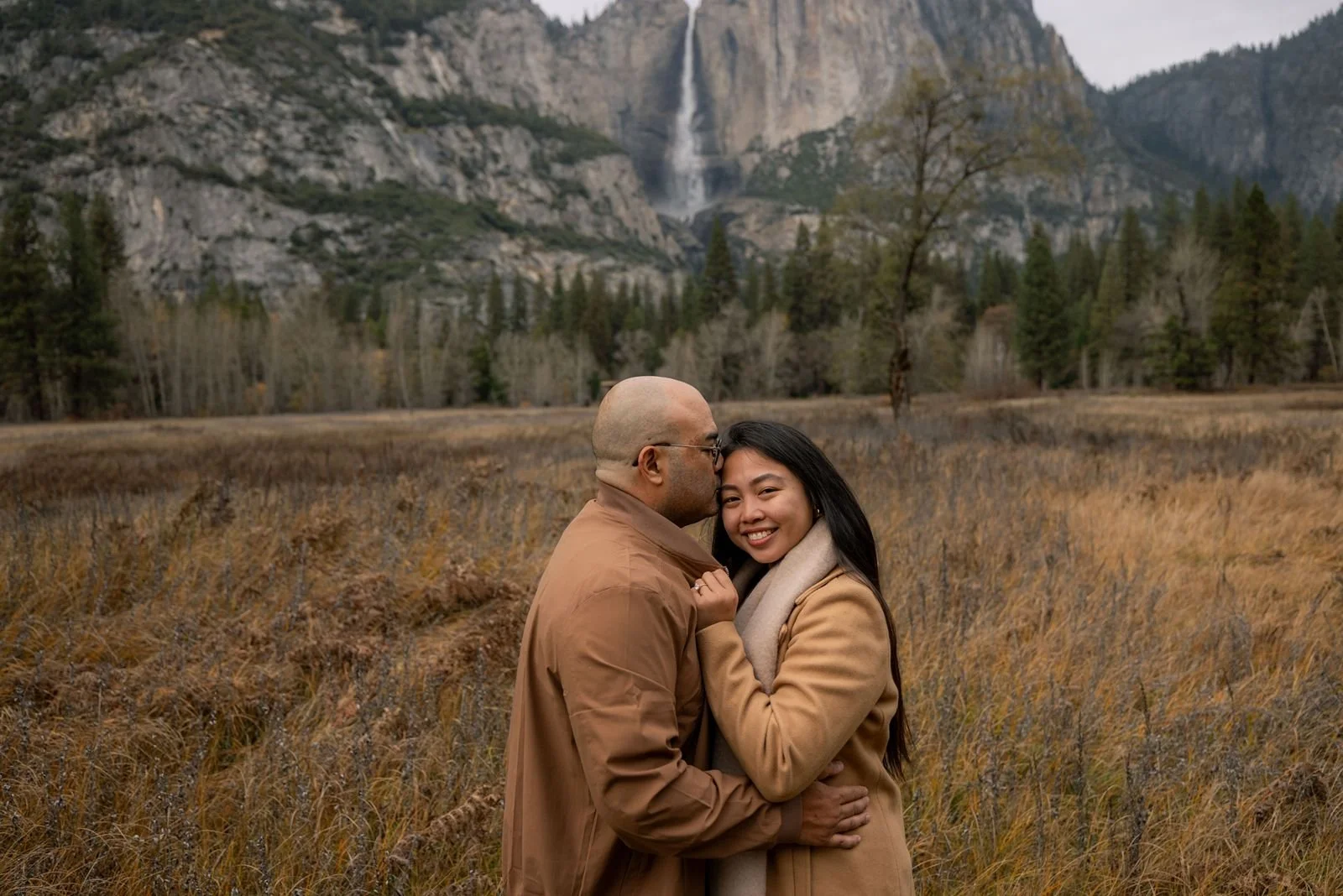Engaged couple kissing in front of a large Yosemite waterfall.