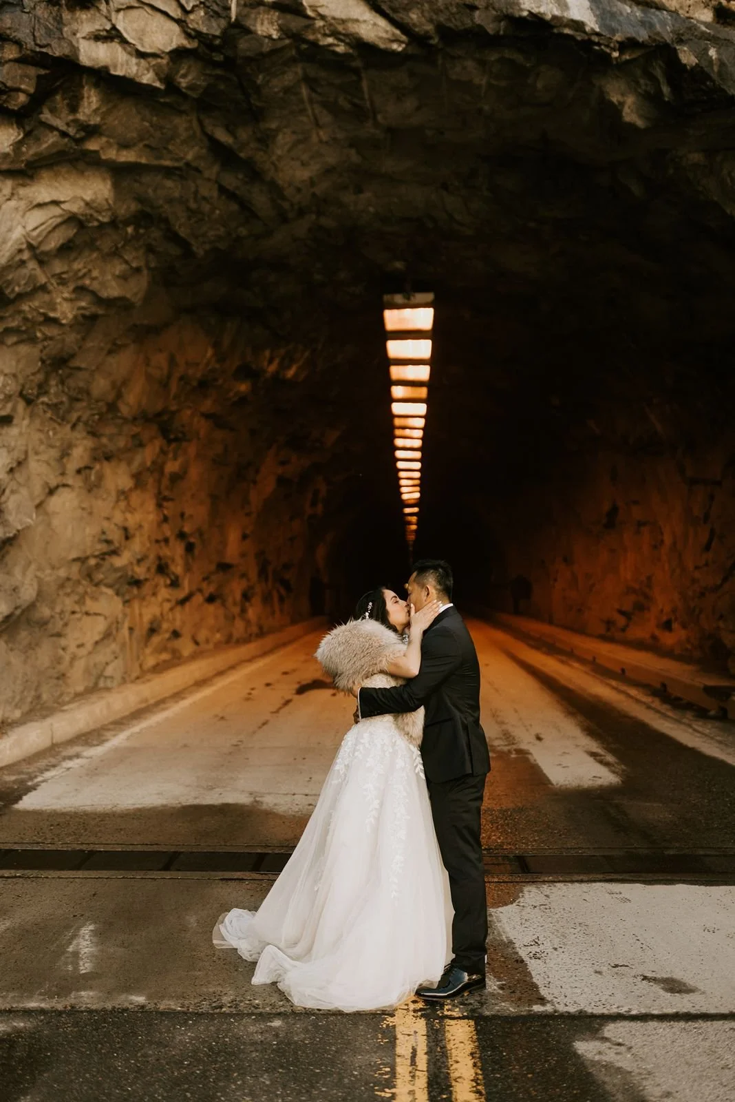 A couple in wedding attire share a kiss under a Yosemite tunnel