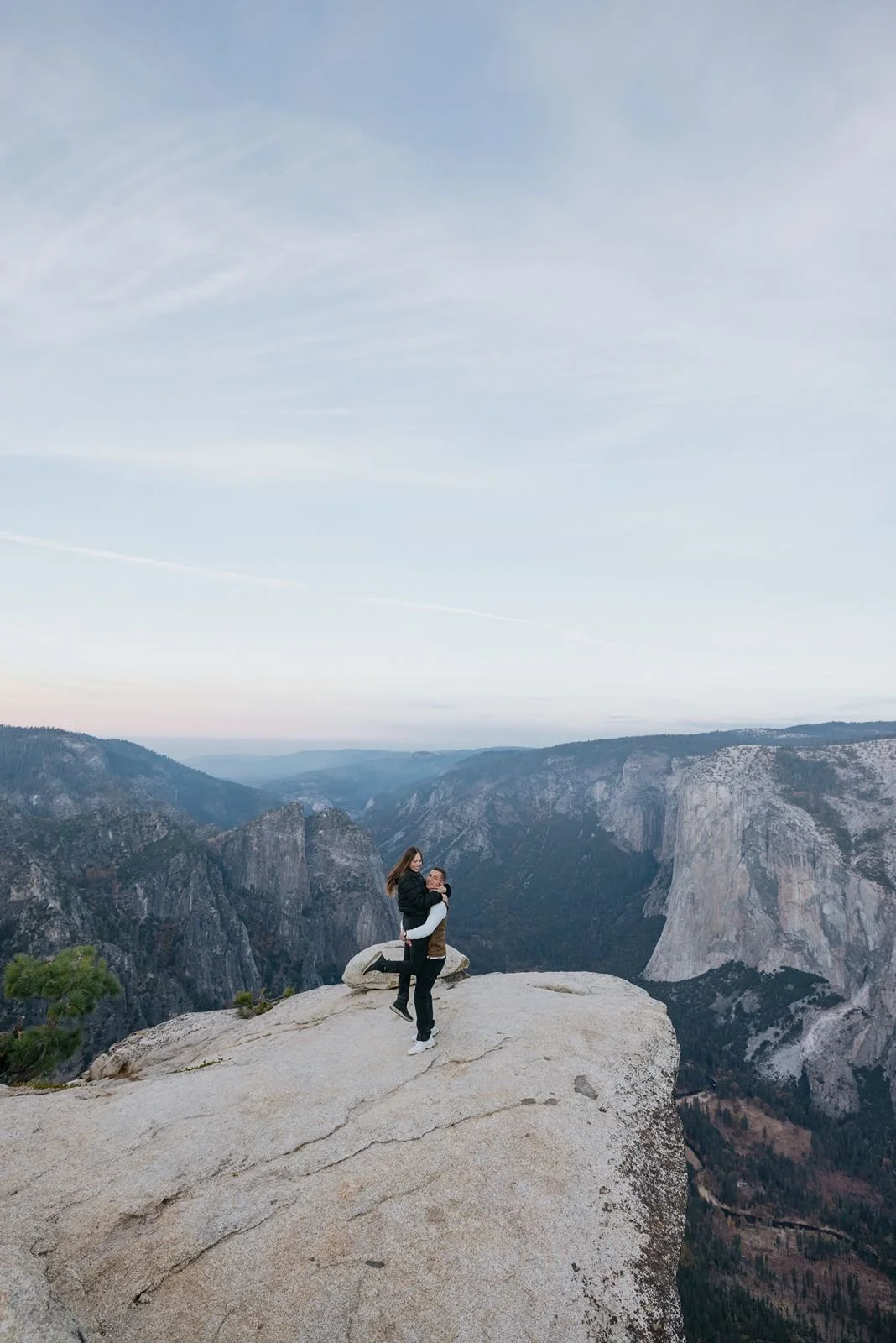 Newly engaged couple hugging at Taft Point in Yosemite National Park during a golden sunrise.