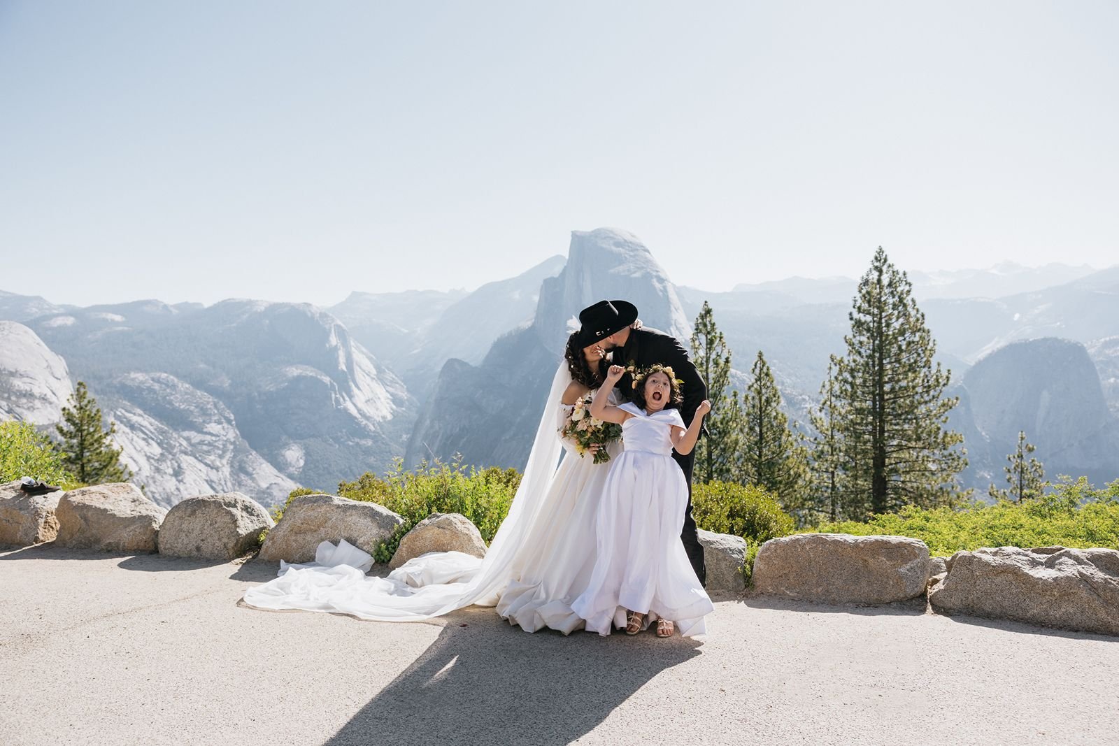 Yosemite photographer Priscilla Banuelos smiling at Glacier Point on her wedding day, while a child jumps in the air out of joy
