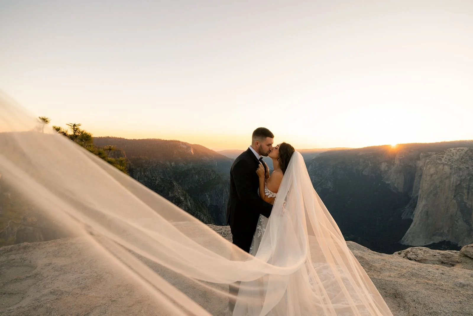 A bride and groom stand together at Taft Point, bathed in golden hour light, showcasing Yosemite's breathtaking scenery.