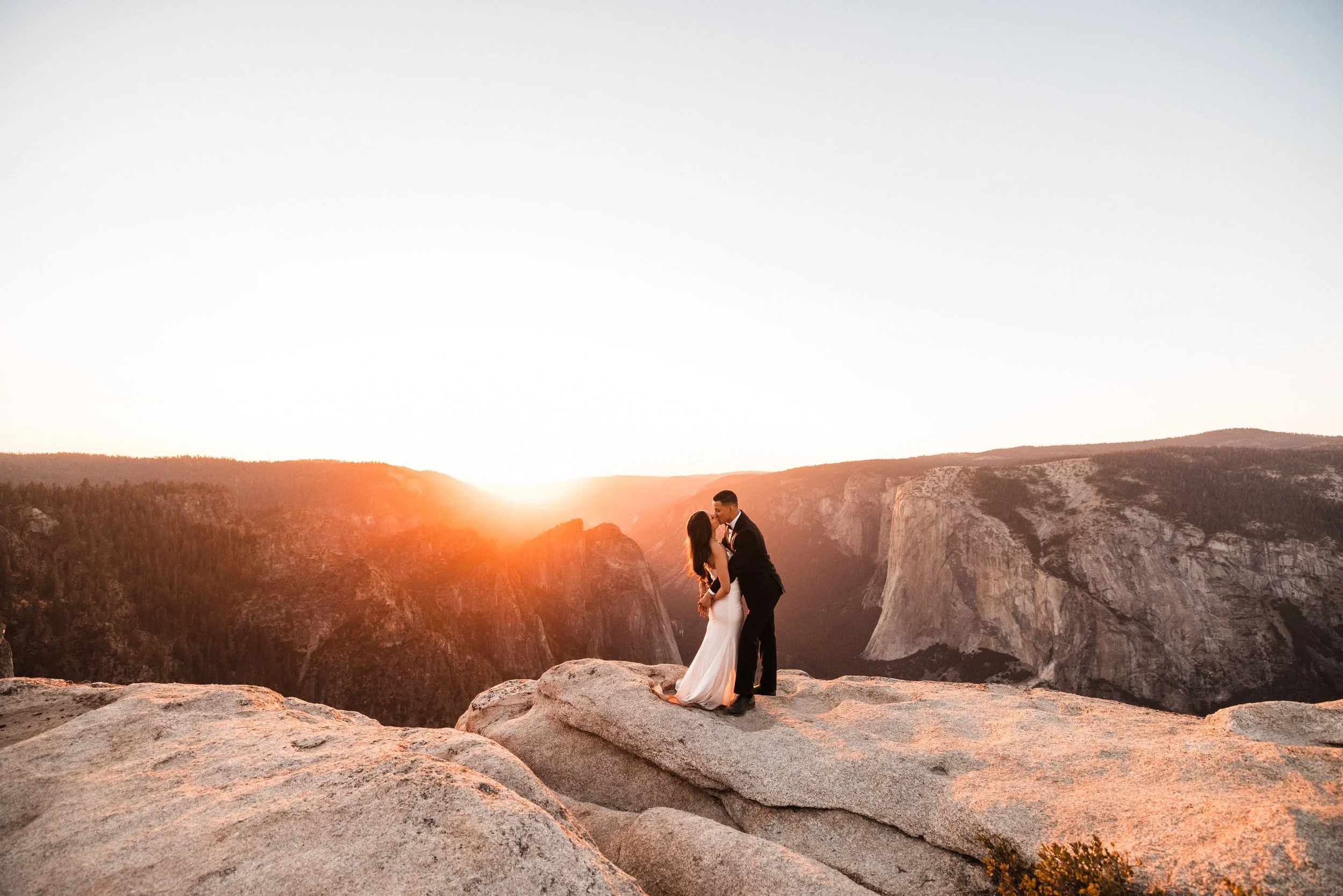 Bride and groom on cliff edge at Taft Point in Yosemite National Park during an orange sunset wedding.