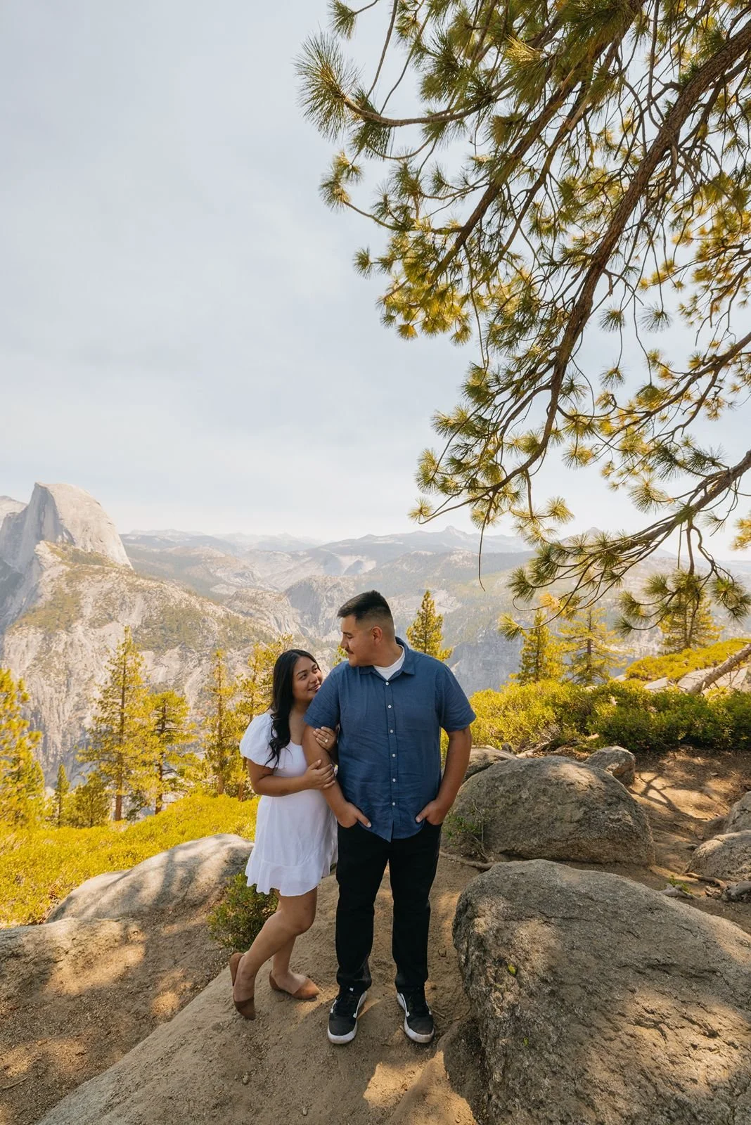 Newly engaged couple smiling and holding each other at the Glacier Point overlook in Yosemite National Park.