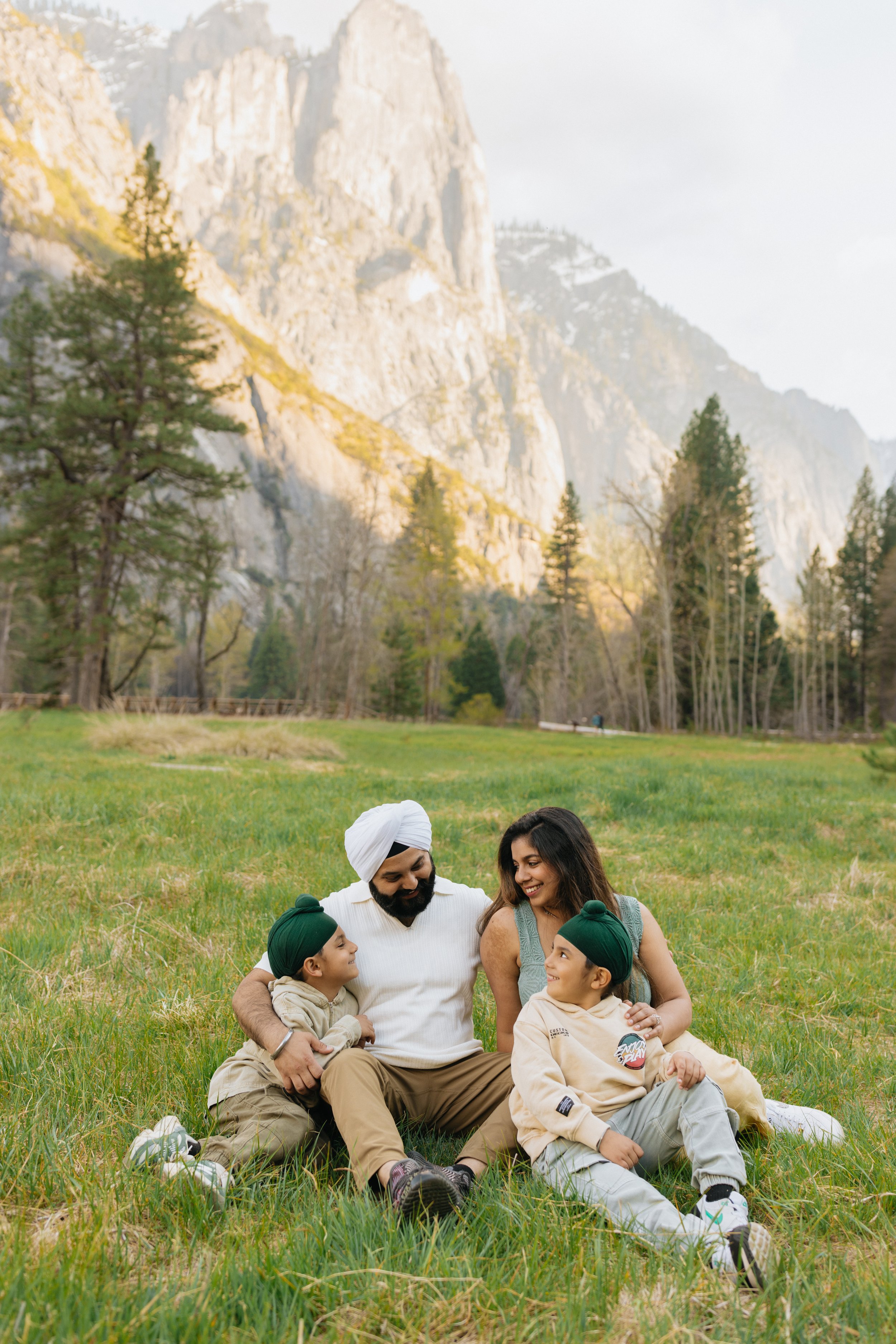 Family of four sitting outdoors in a green field with snowy mountain tops in Yosemite National Park.