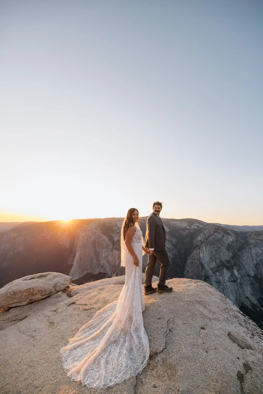 A couple in wedding attire hold hands at the top of Taft point at sunset