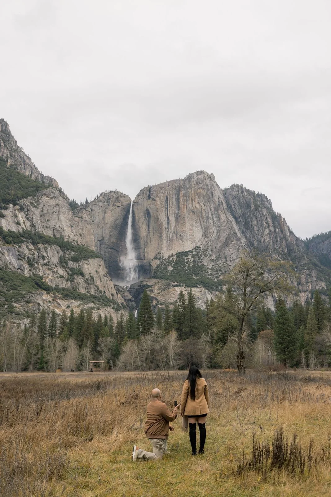 Man proposing to his fiancé with a large Yosemite waterfall in the background.