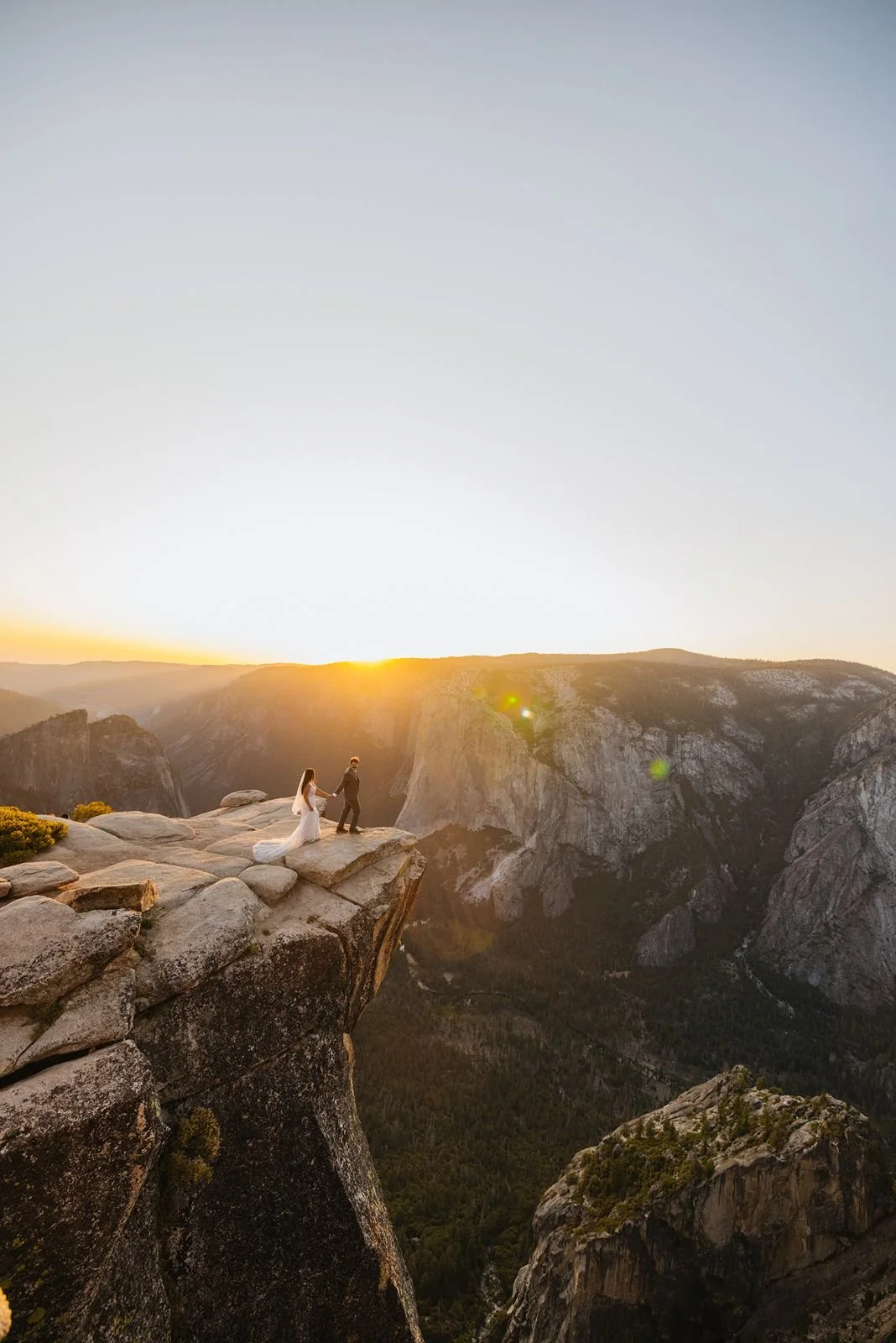 A bride and groom hold hands at the edge of Taft Point at sunset