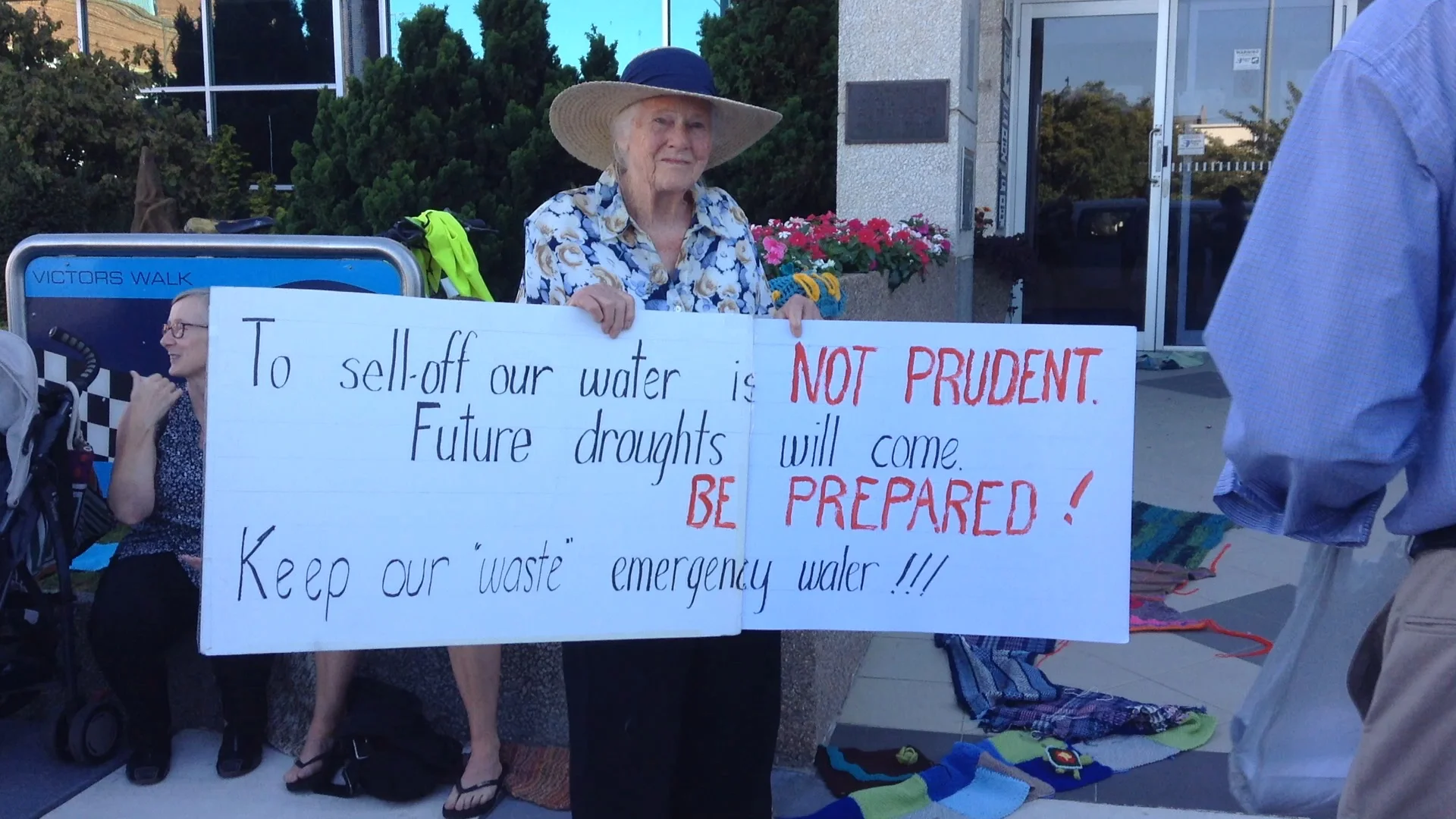 Isabel Higgins with a hand-written sign outside council chambers, Feb 2016. The yarned river can be seen snaking towards the door of council chambers. Photo by Tracy Sorensen.