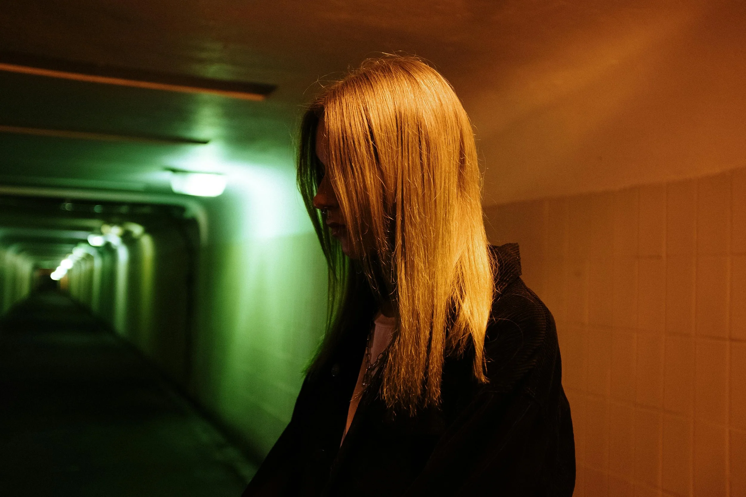 A person standing in a passageway lit in warm amber and green.