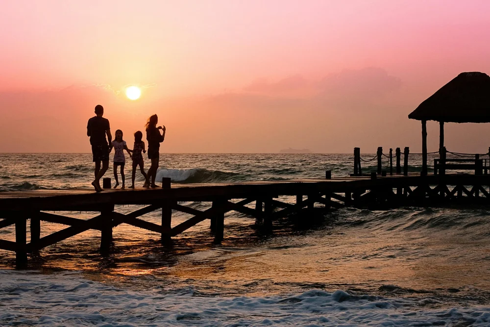 A family together on a pier beside the water at sunset.